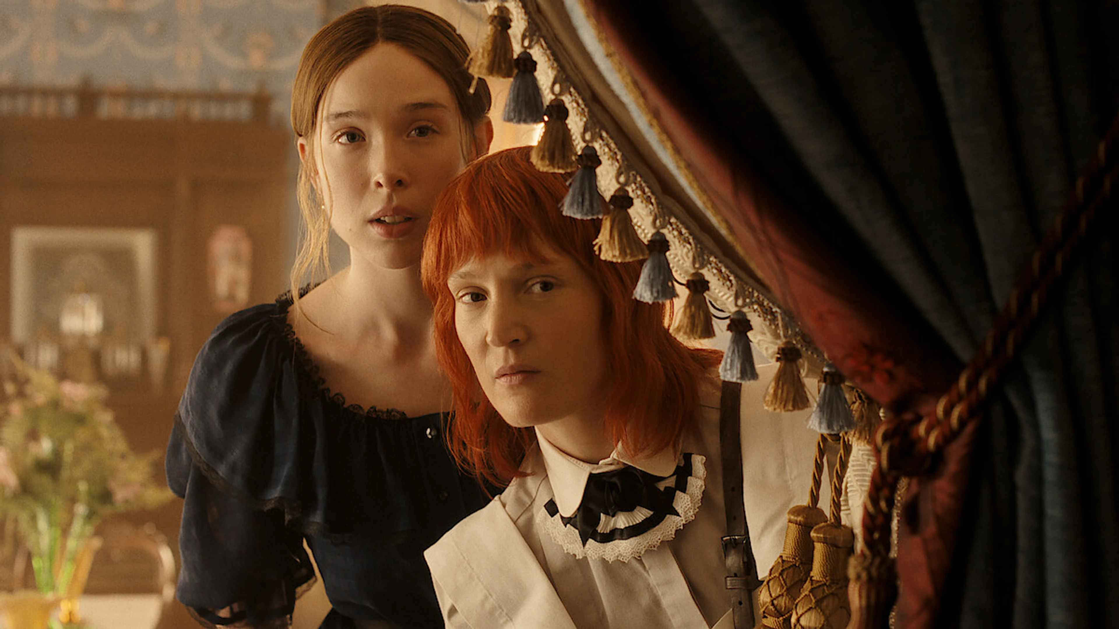 Lizzie Borden and Bridget Sullivan look out from behind a curtain in period dress.