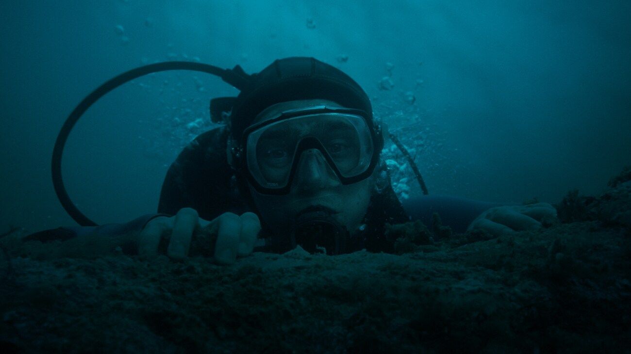 Jay Gardiner grips the edge of a submerged surface in his diving mask.
