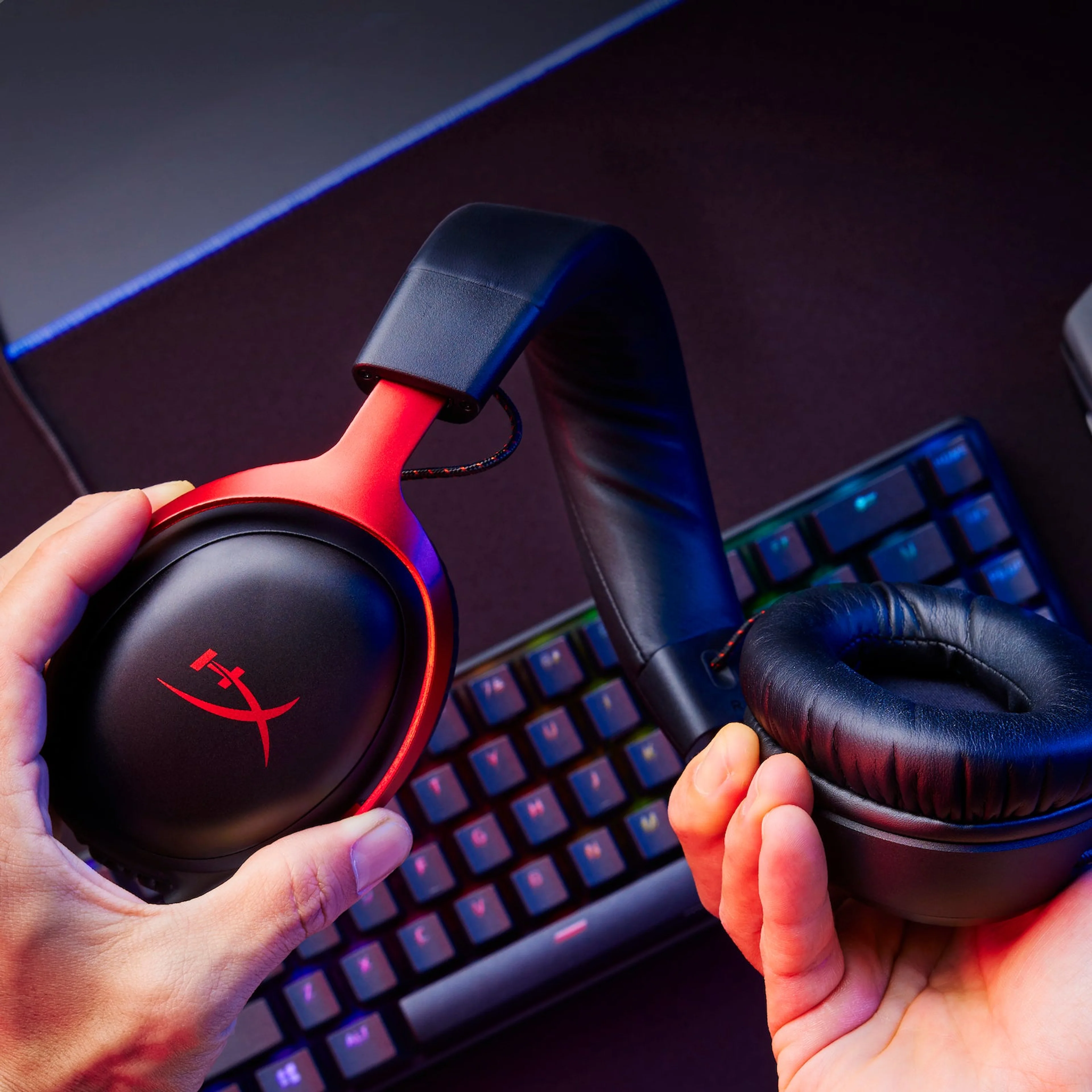 Black and red HyperX Cloud III held above a gaming keyboard, showing its padded earcups and metal frame