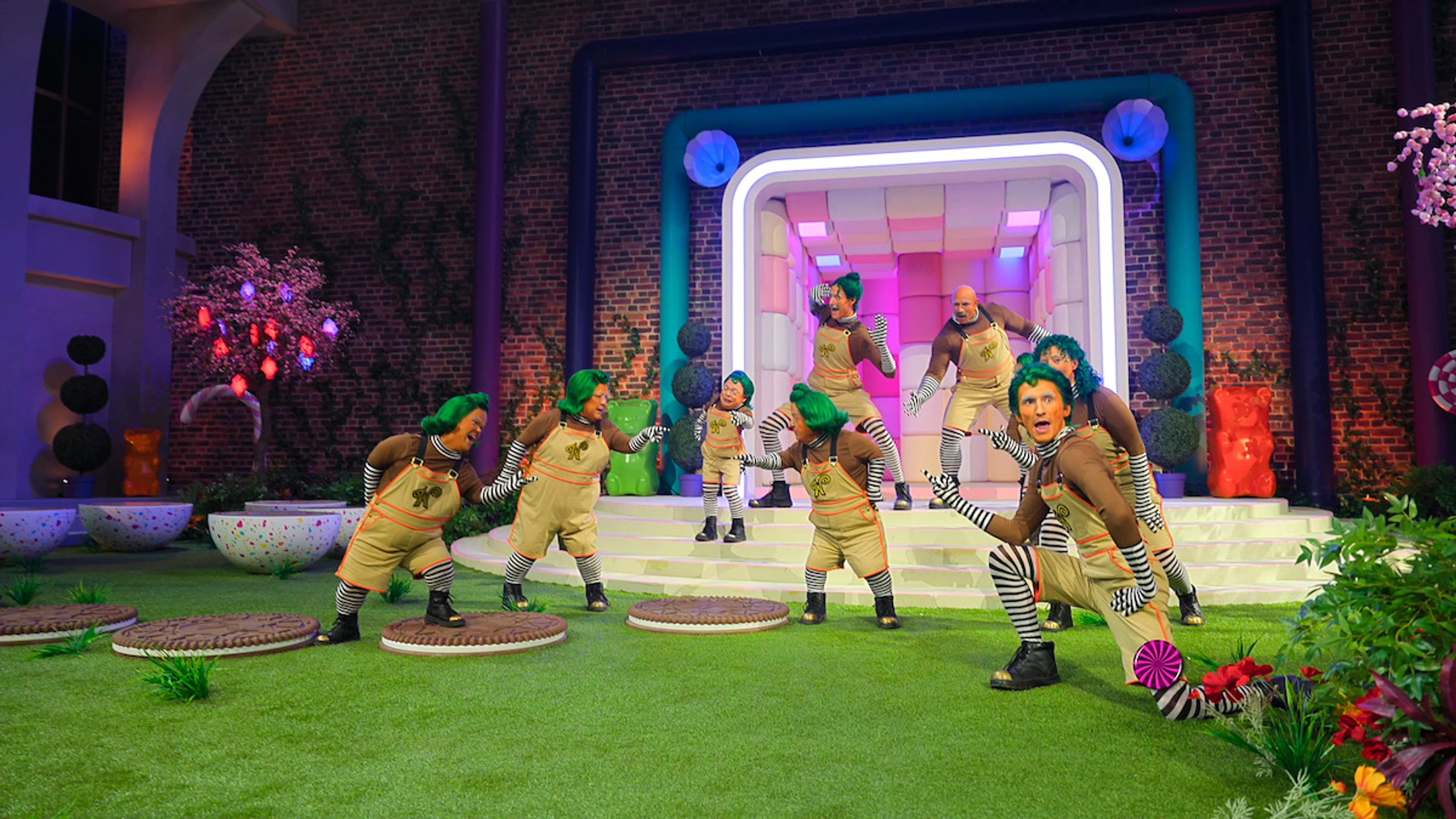 Oompa-Loompa performers pose on a colorful factory set.