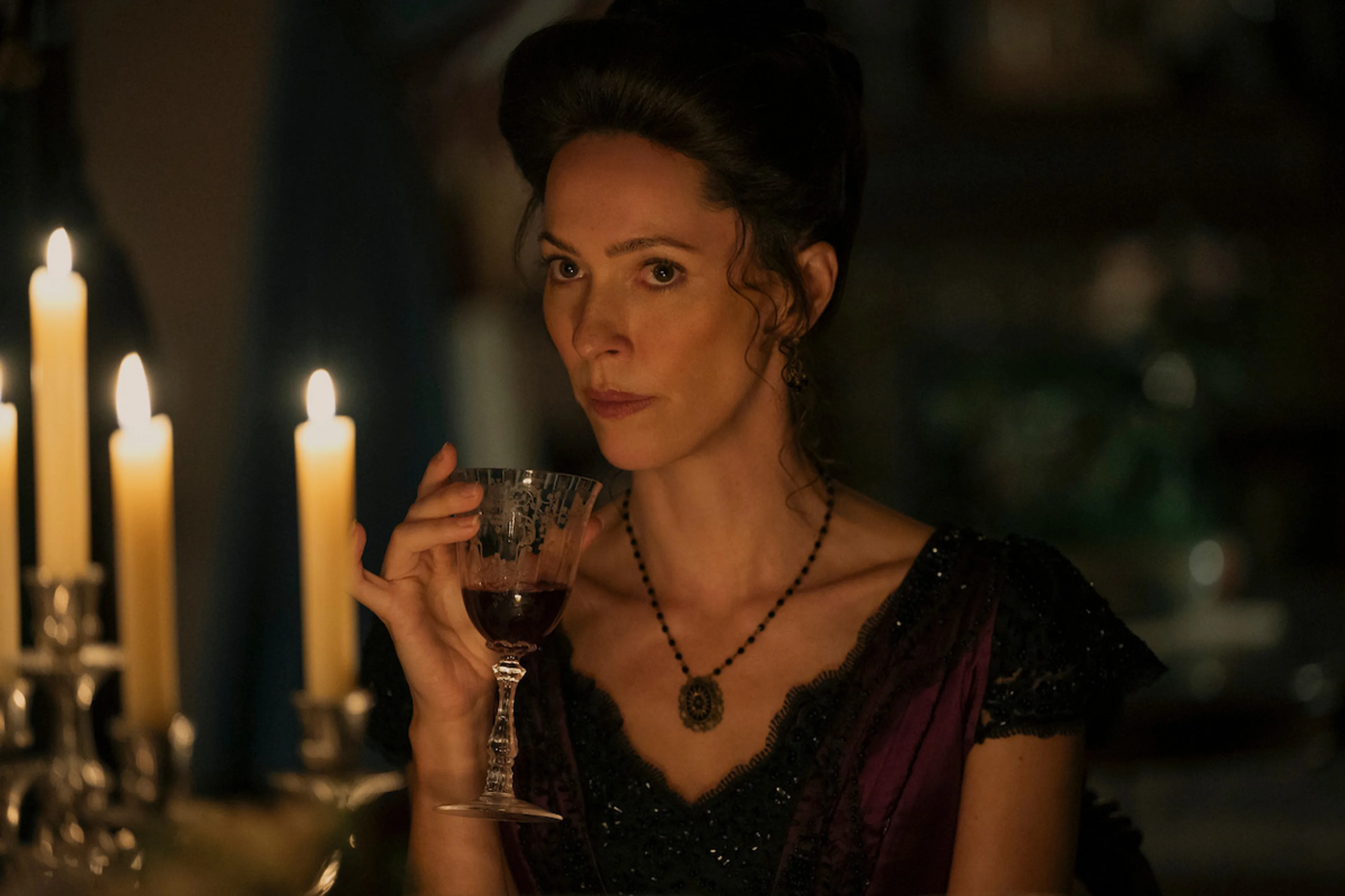 A woman in period clothing sits beside candlelight in Monster: The Lizzie Borden Story.