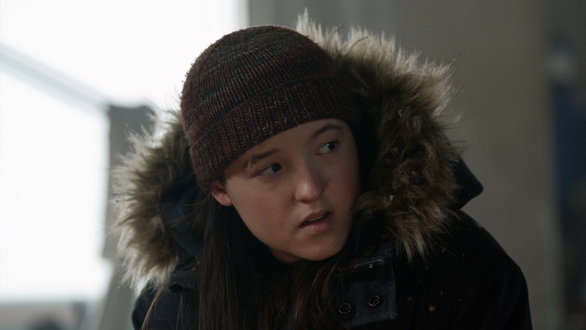 Ellie looks to her right while wearing a knit hat and winter coat in The Last of Us.