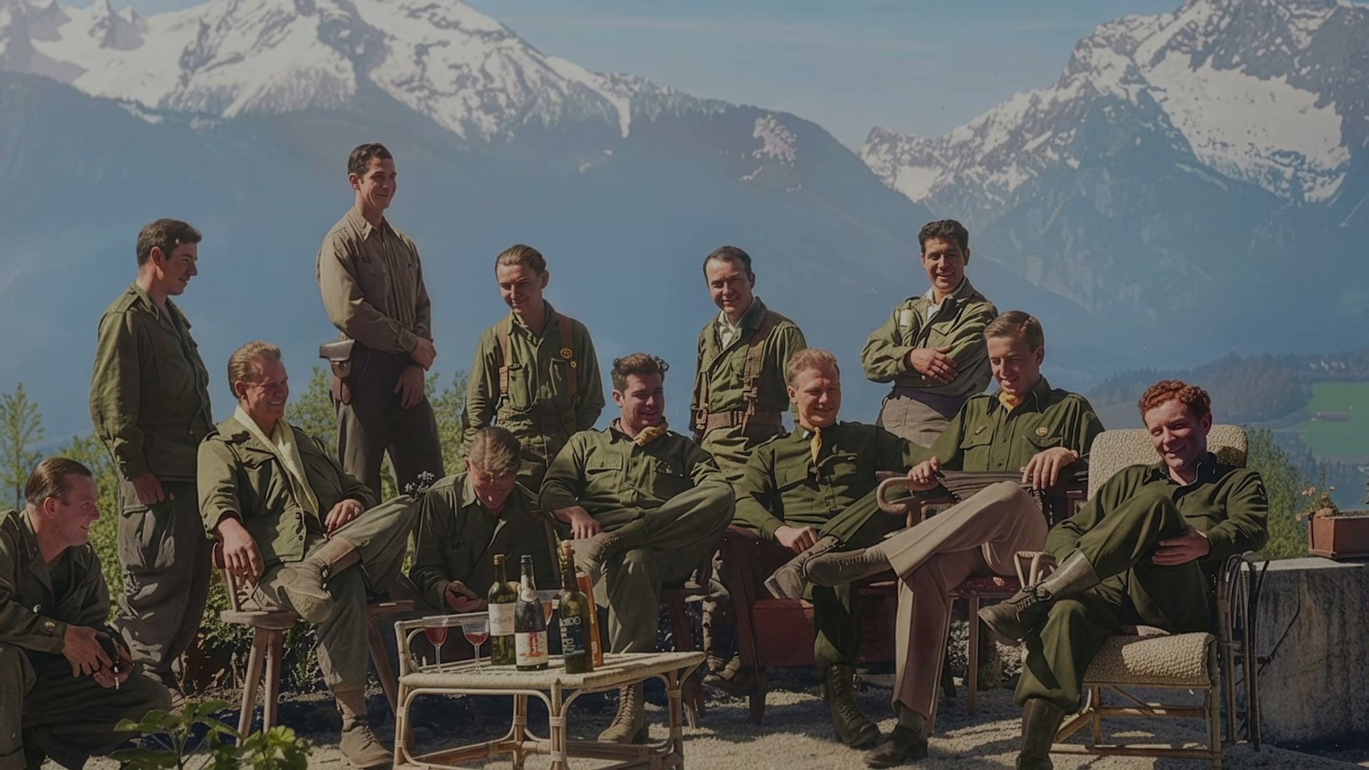 Members of the Band of Brothers cast gather outdoors in uniform with mountains behind them.