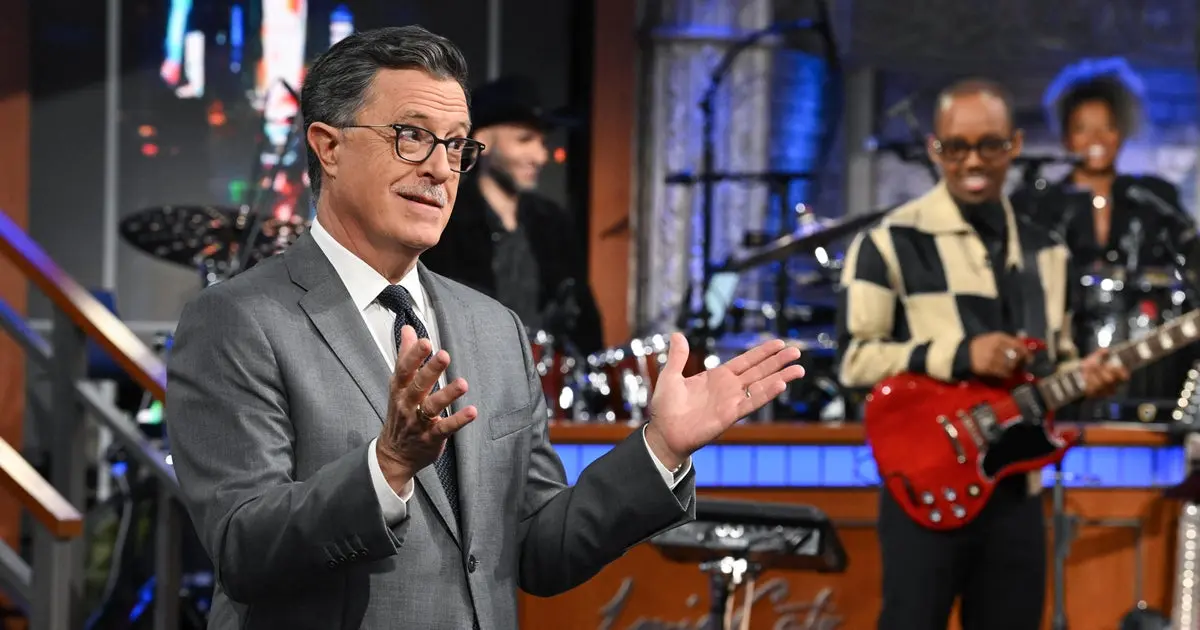 Stephen Colbert gestures on the set of The Late Show as the band performs behind him.