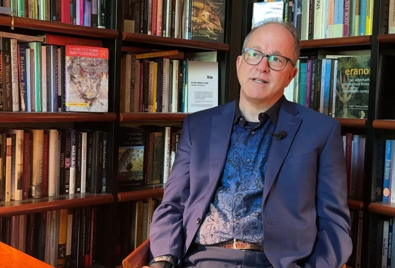 Archive X host Jeffrey J. Kripal sits in front of bookshelves.