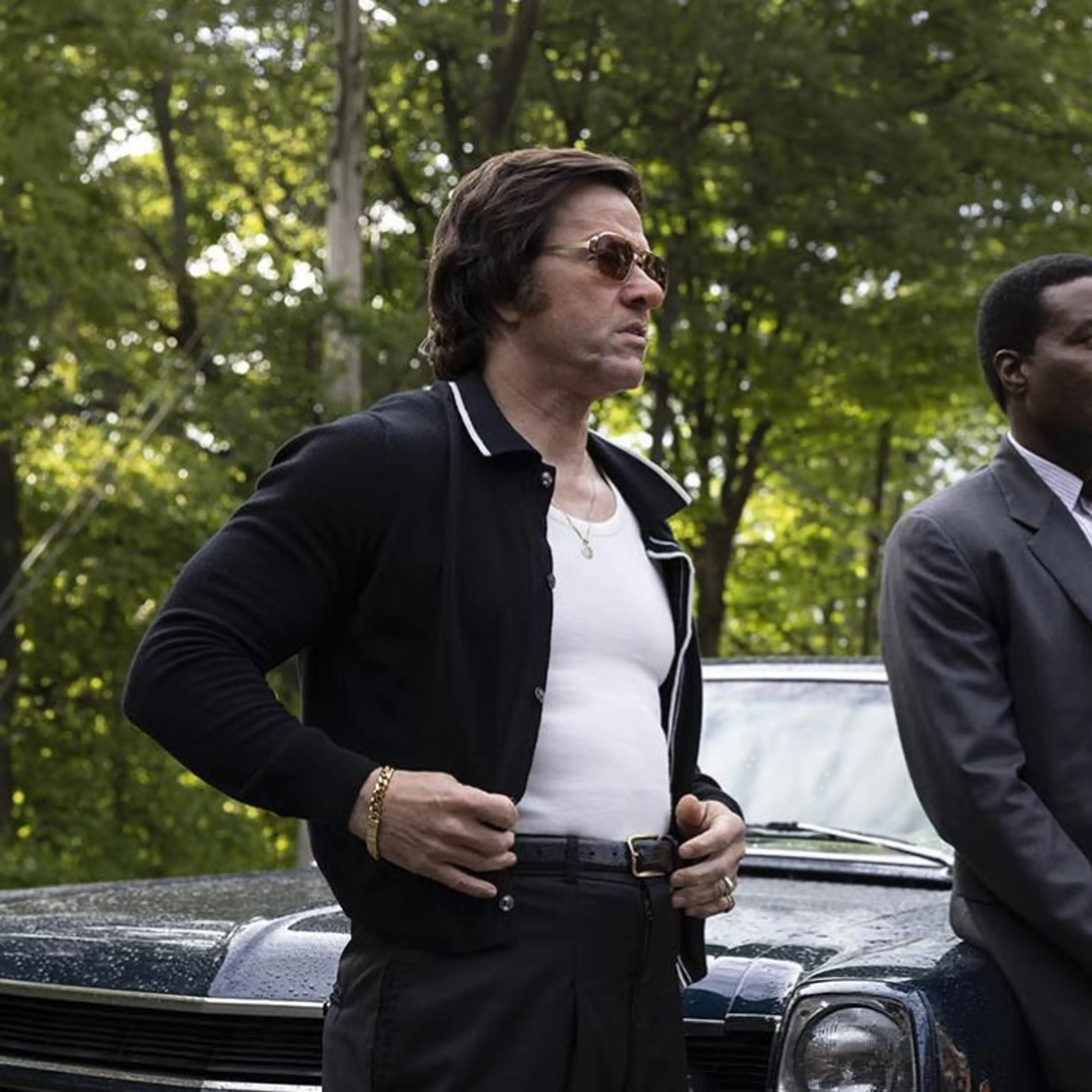 Yahya Abdul-Mateen II and Mark Wahlberg stand beside a car on a wooded road in By Any Means.