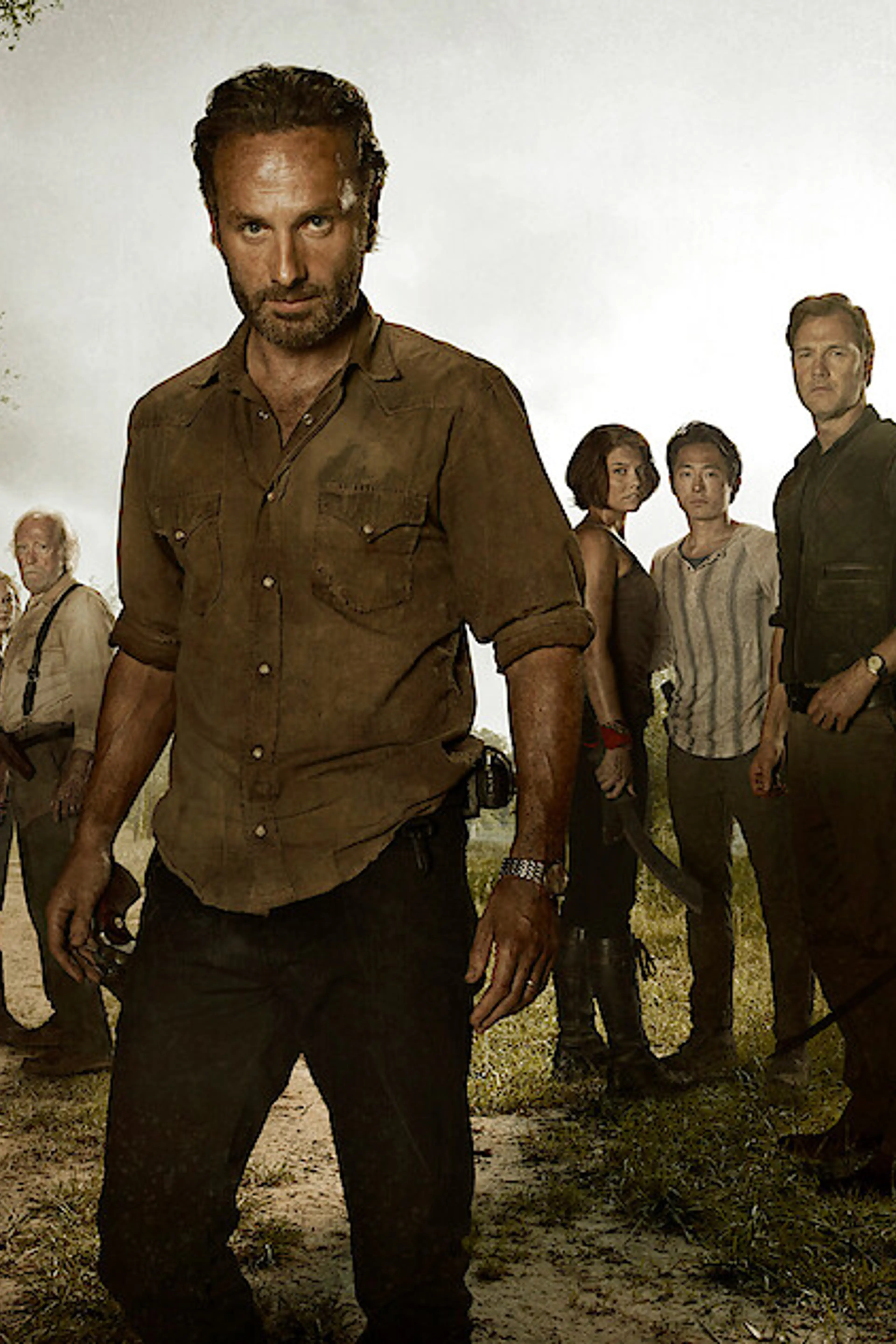 Rick Grimes stands in front of an ensemble of The Walking Dead survivors.