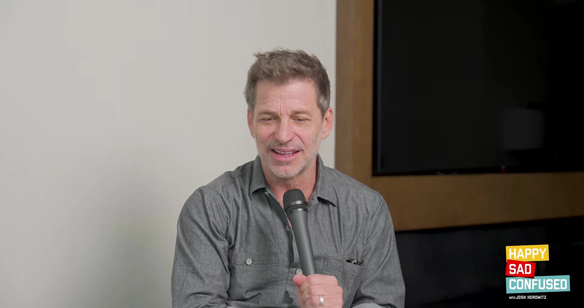 Zack Snyder holds a microphone during an interview with Josh Horowitz.