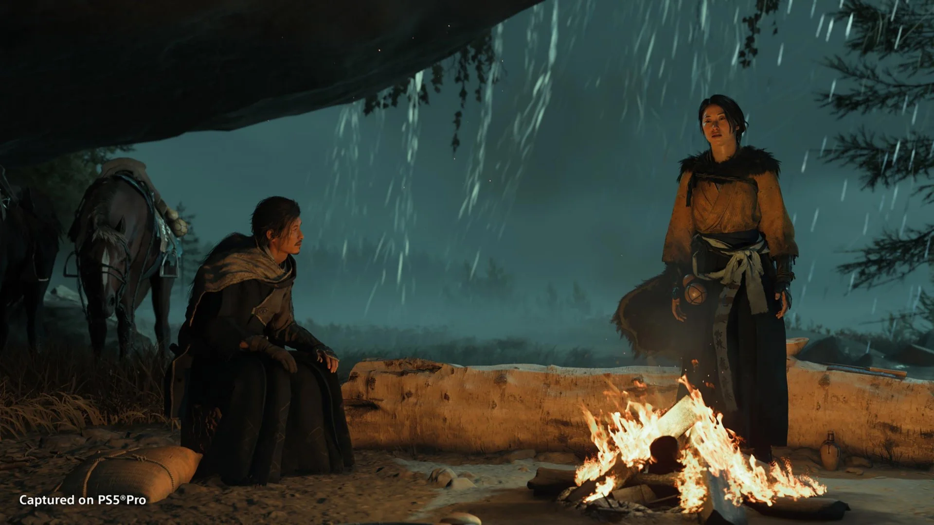 Atsu and another warrior shelter from rain beside a campfire, with a horse nearby.