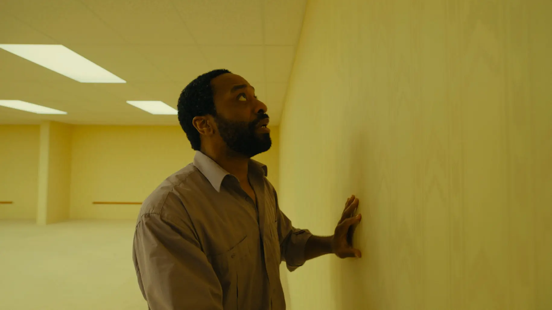 Chiwetel Ejiofor as Clark touches a yellow wall in Backrooms.