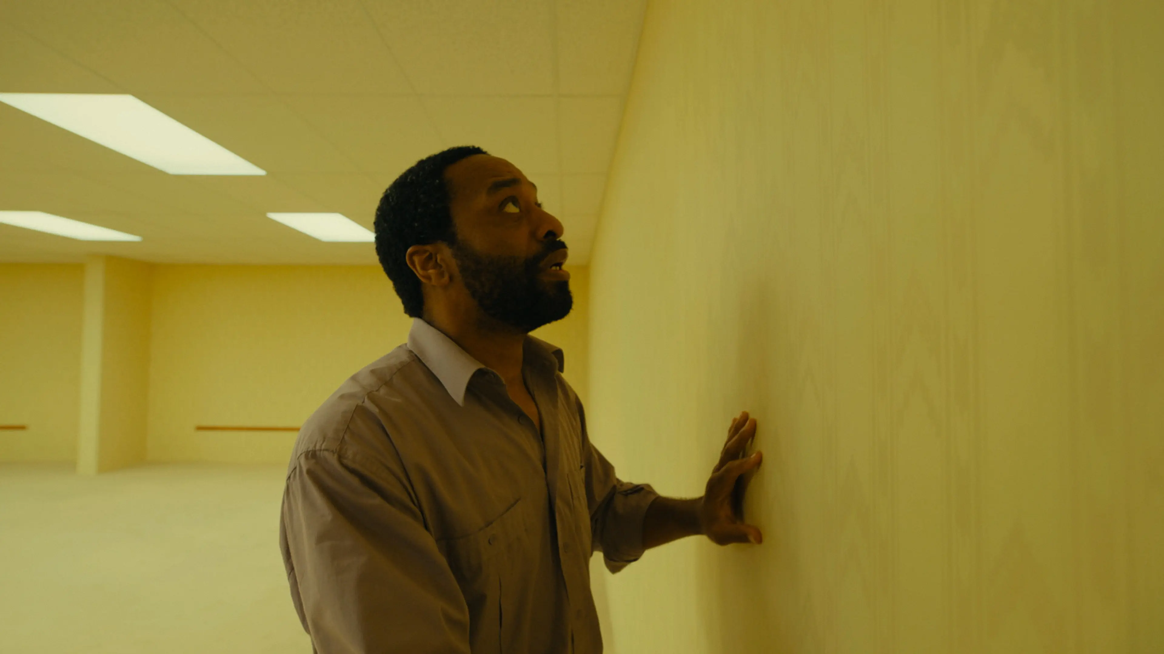 Chiwetel Ejiofor as Clark touches a yellow wall in Backrooms.