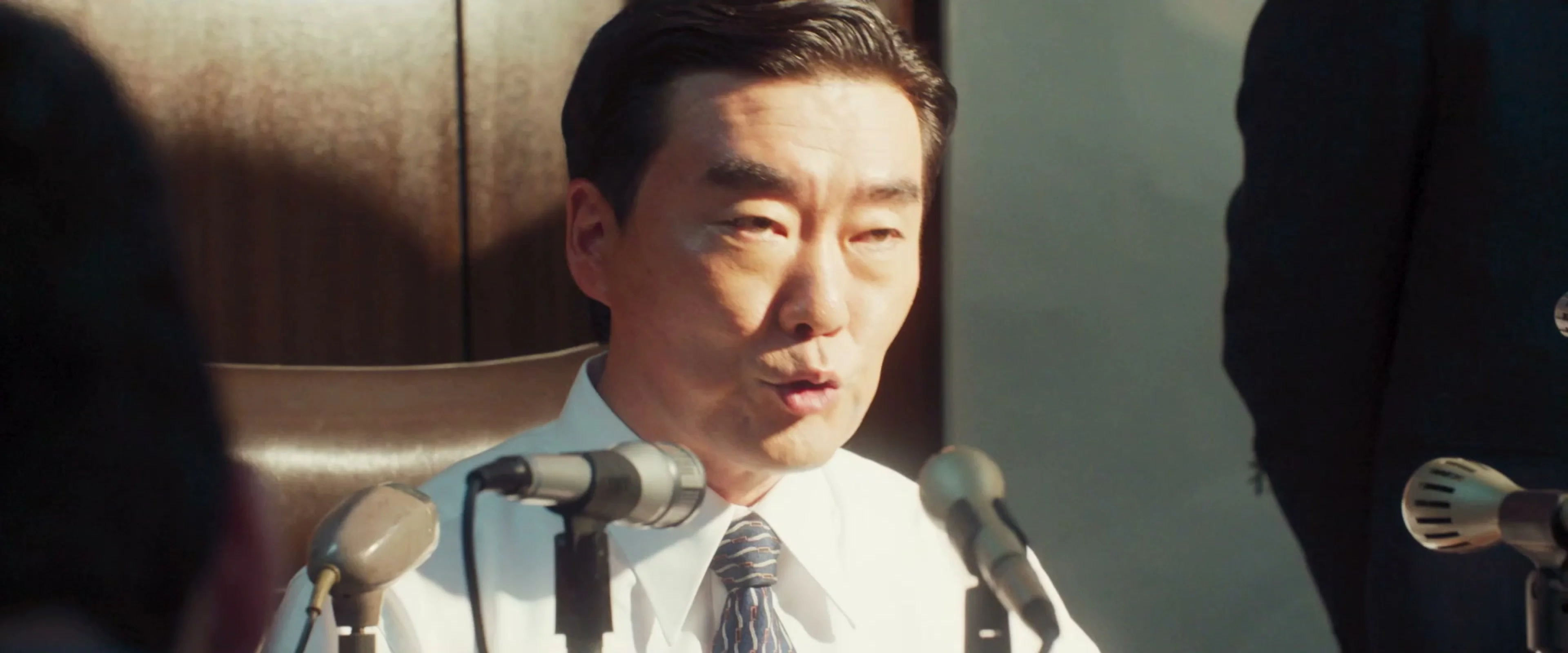 A man speaks into several microphones in a clean frame from The Assassin(s) trailer.