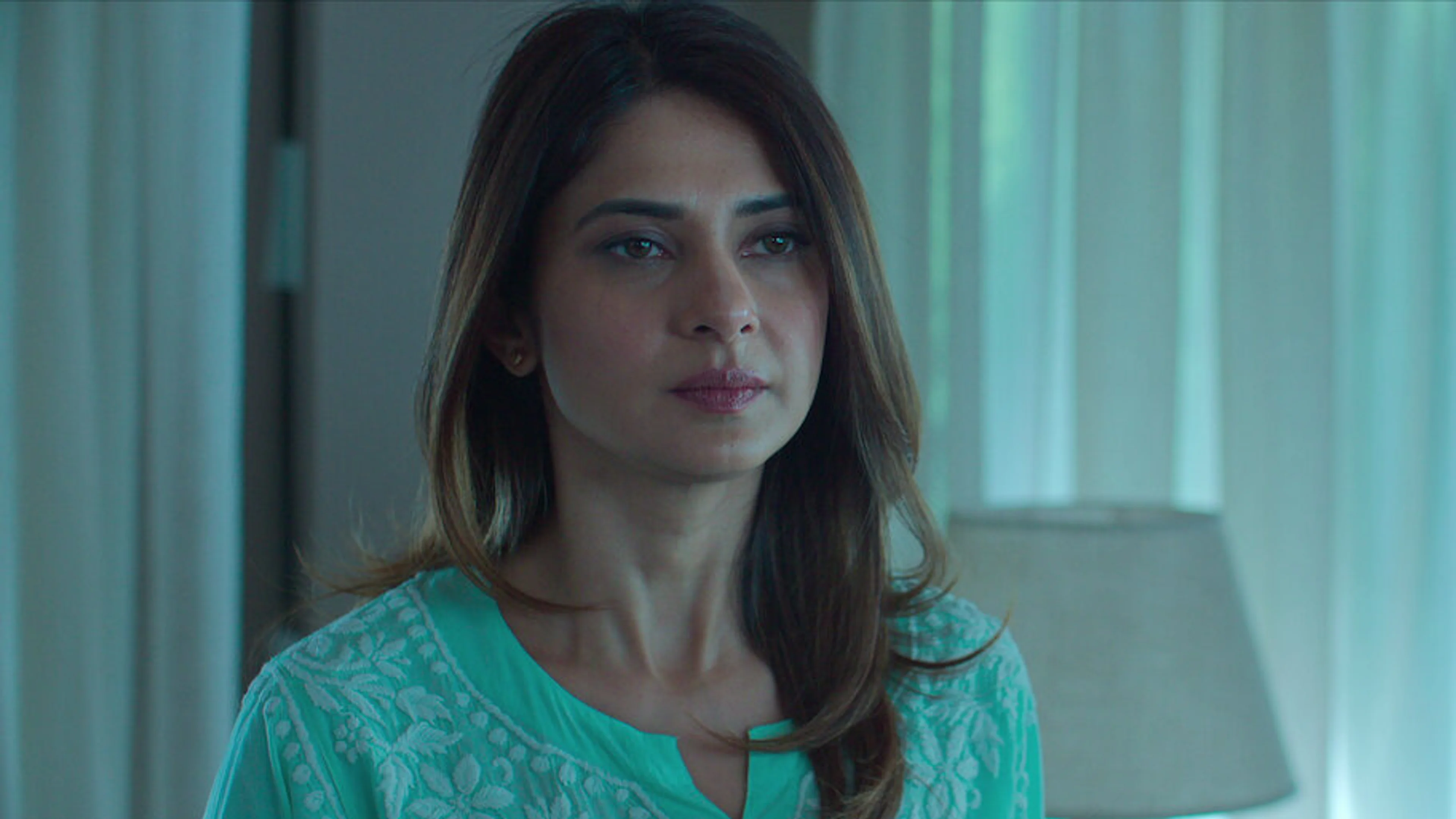 A woman sits in a blue-lit room in the Shaque: Trust No One teaser.
