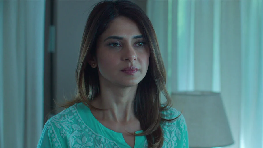 A woman sits in a blue-lit room in the Shaque: Trust No One teaser.