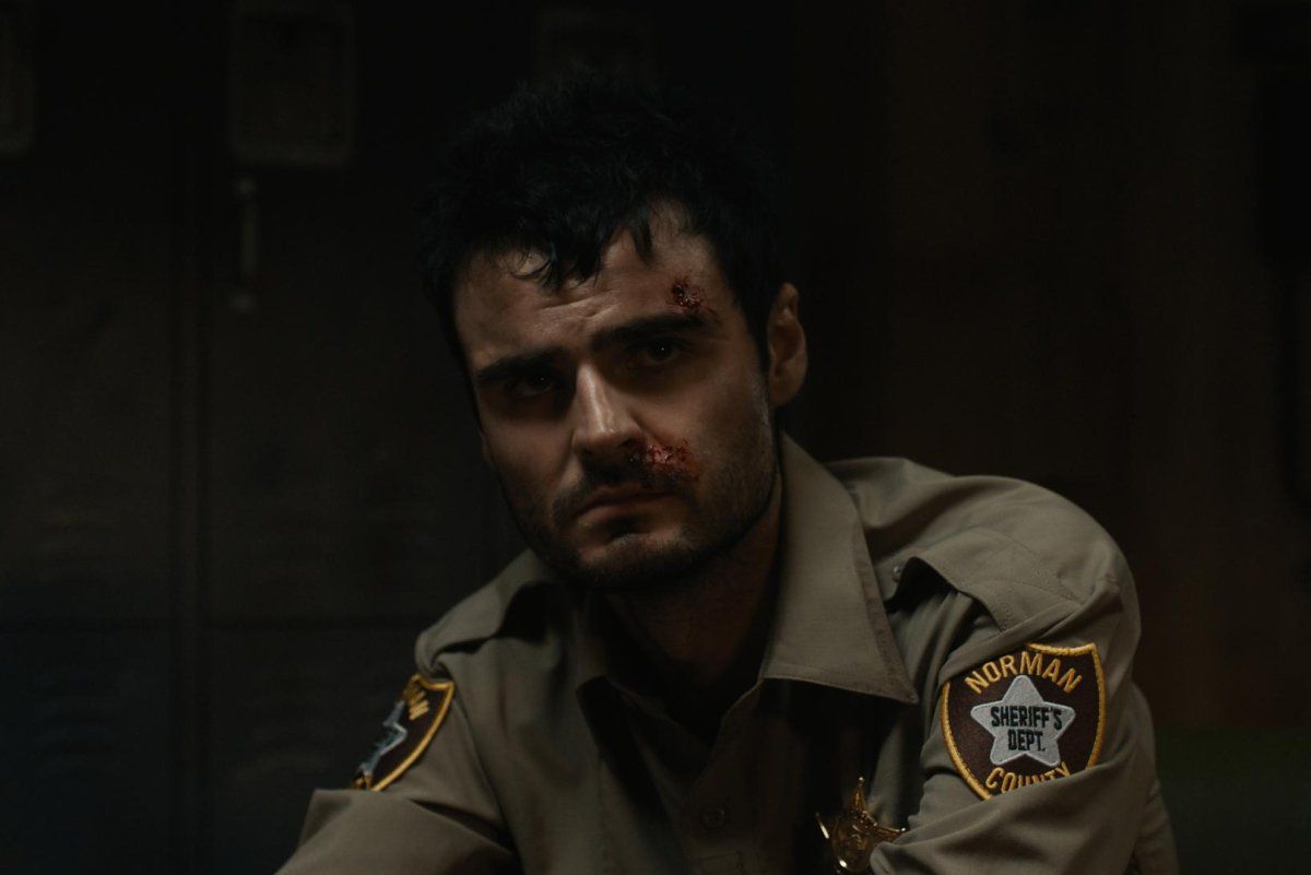 A bruised Duke Nicholson wears a sheriff’s uniform in a dark room.