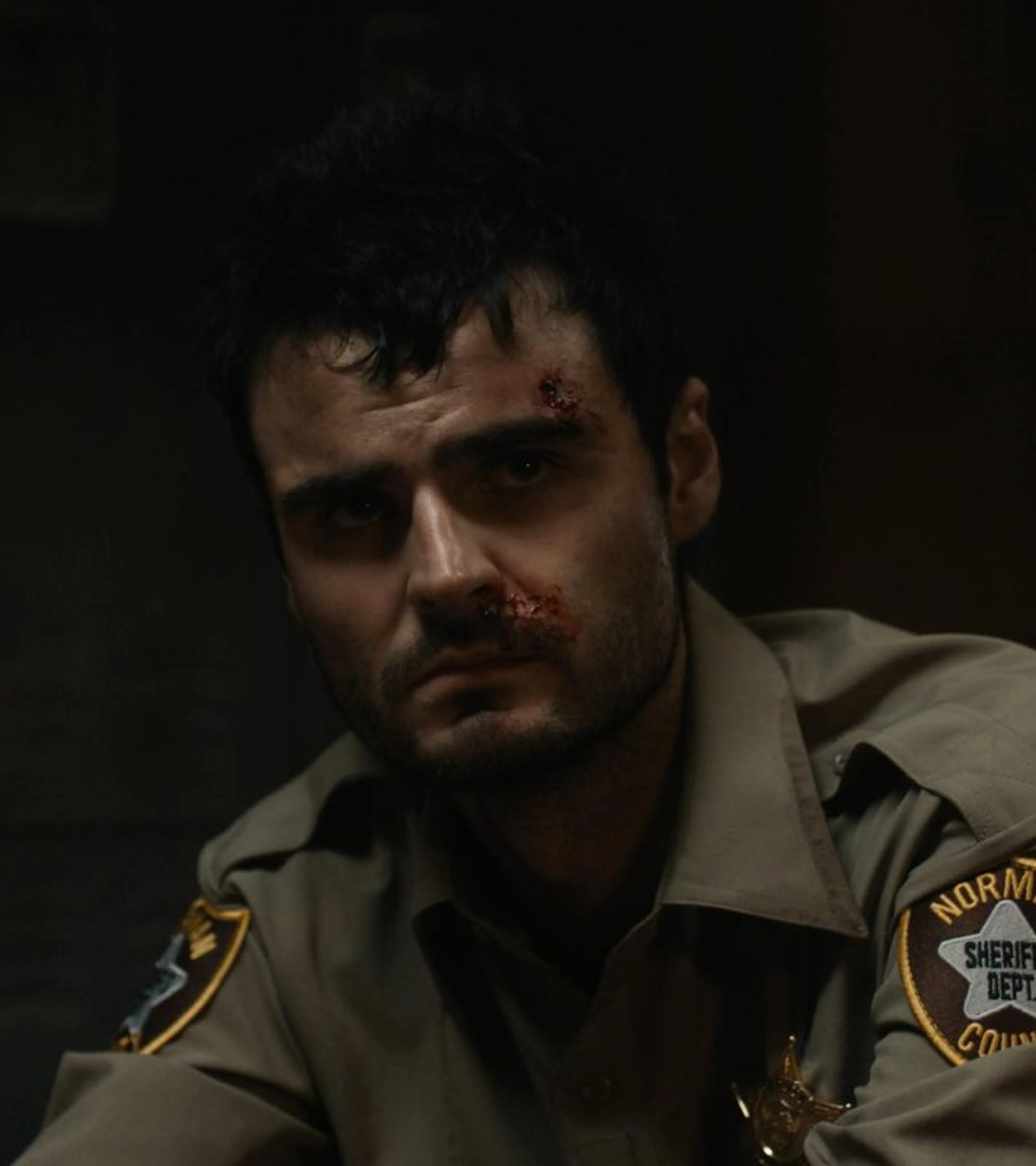 A bruised Duke Nicholson wears a sheriff’s uniform in a dark room.