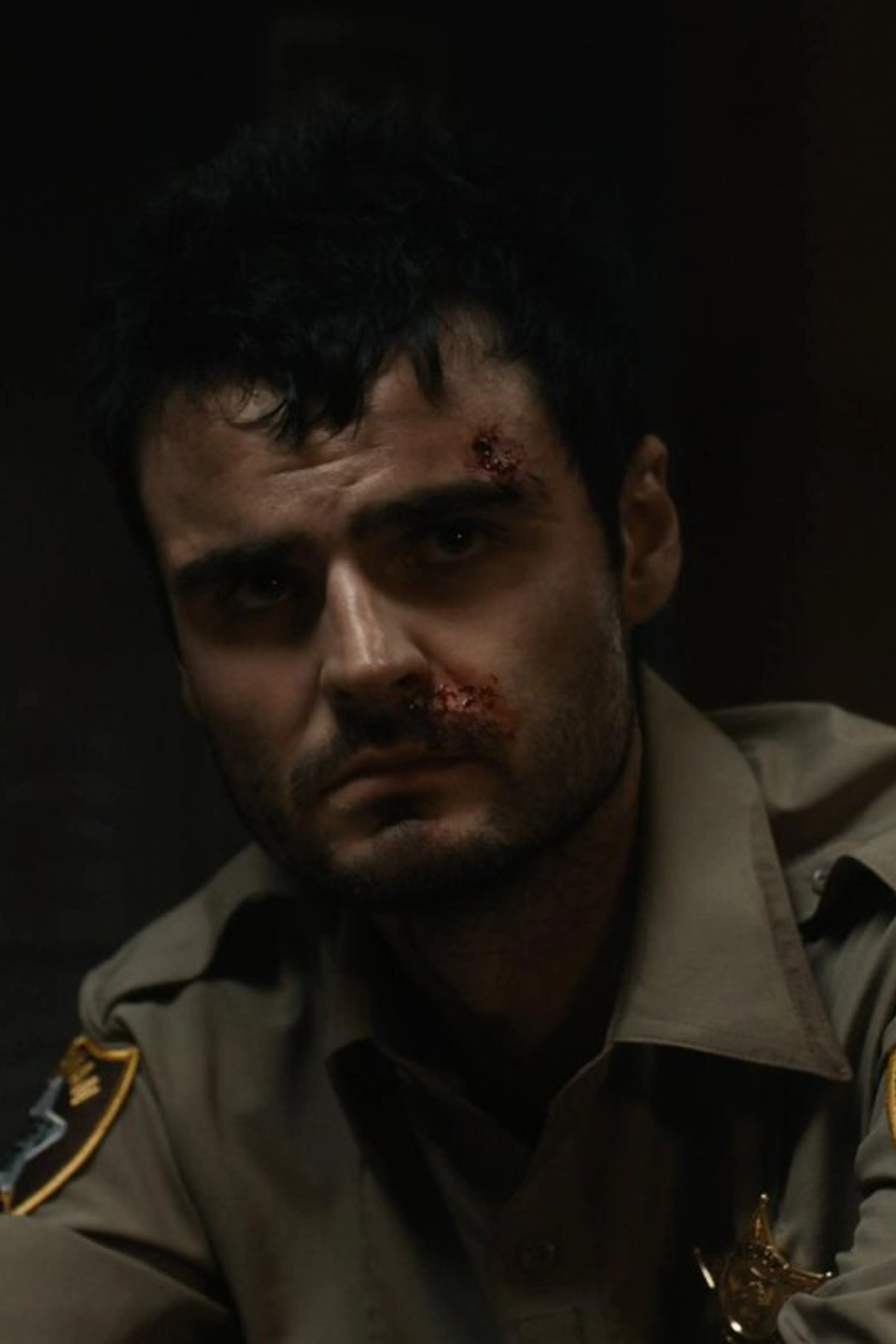 A bruised Duke Nicholson wears a sheriff’s uniform in a dark room.