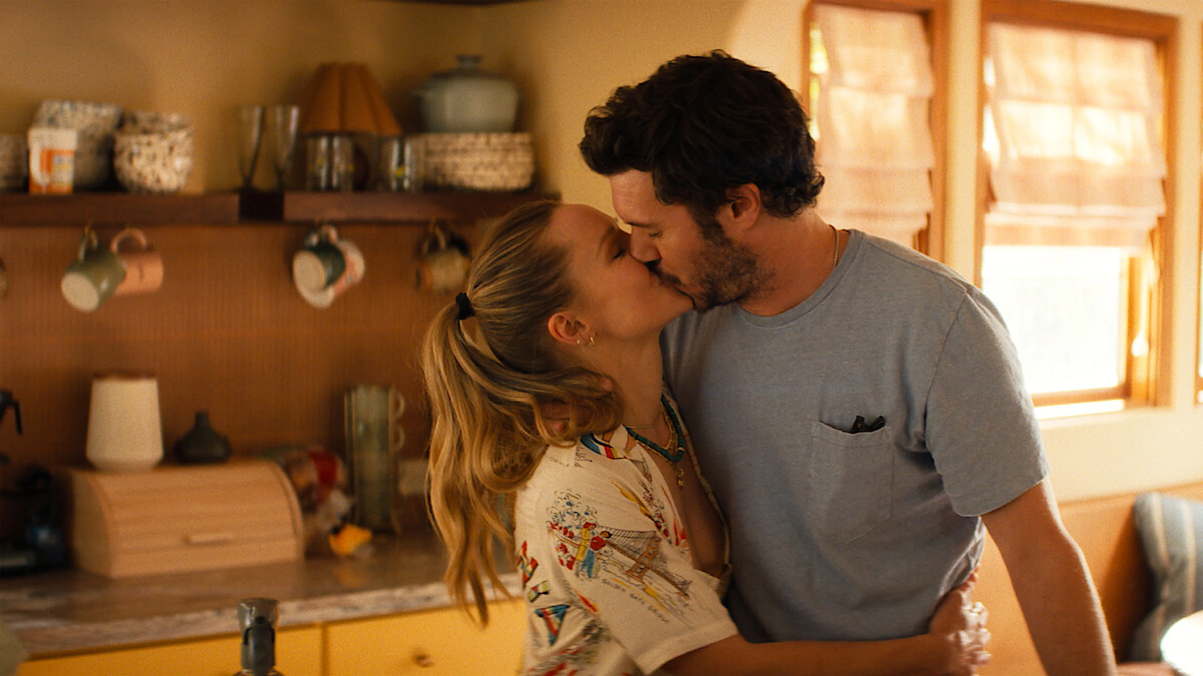 Kristen Bell as Joanne and Adam Brody as Noah kiss in a sunlit kitchen in Nobody Wants This Season 3.