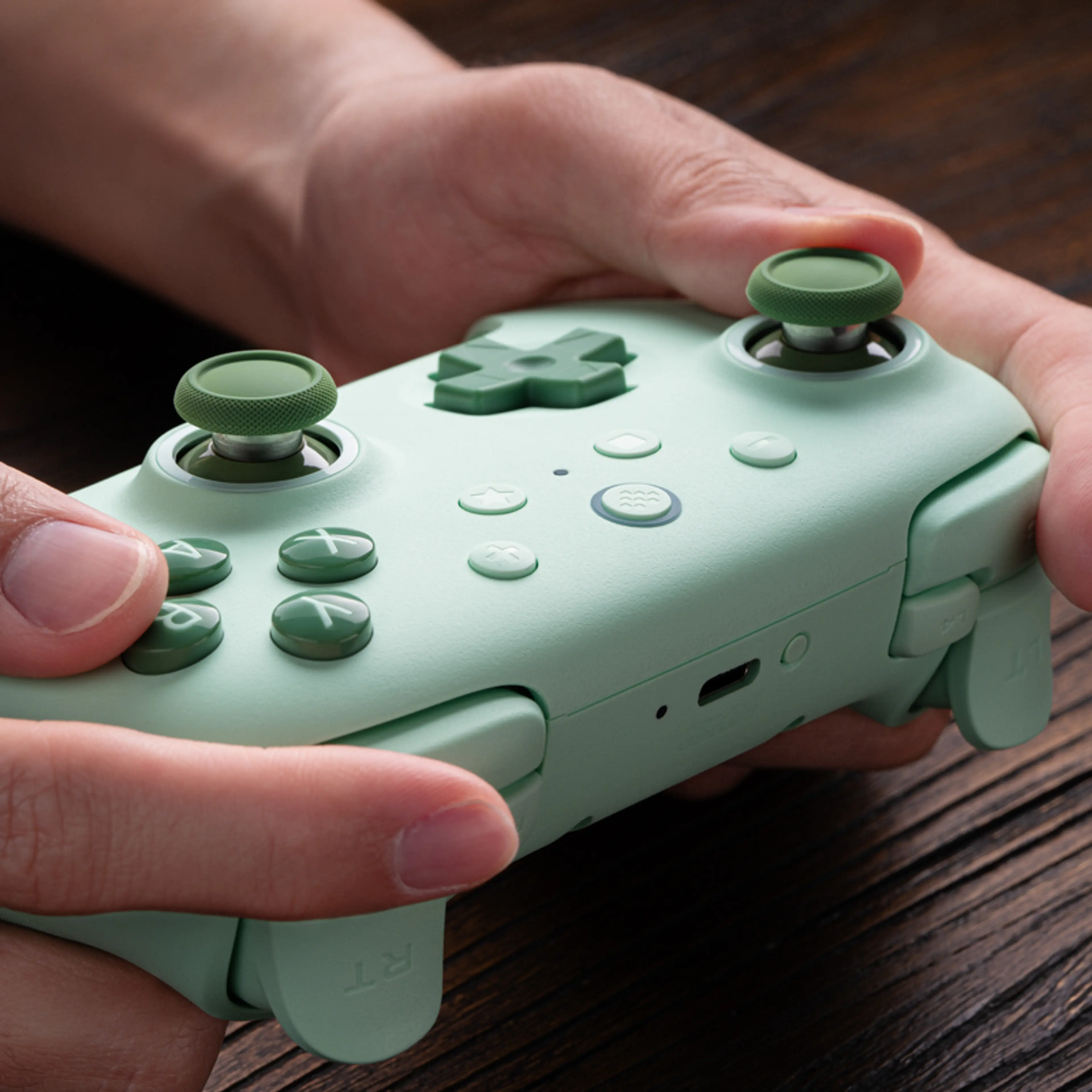 Green 8BitDo Ultimate 2C Wireless held in two hands, showing its buttons and USB-C port