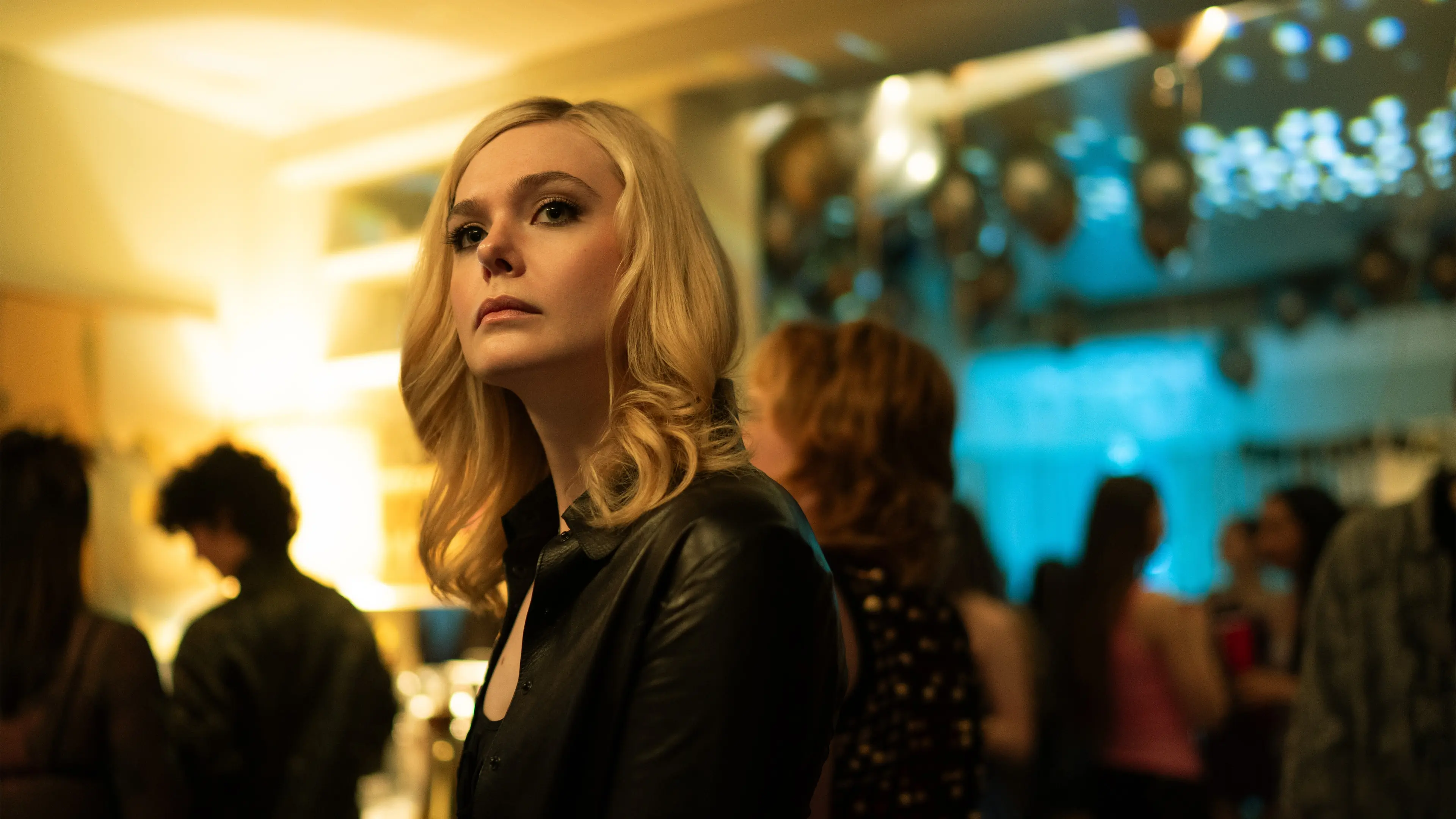 Elle Fanning as Margo wears a dark jacket at a party with balloons.
