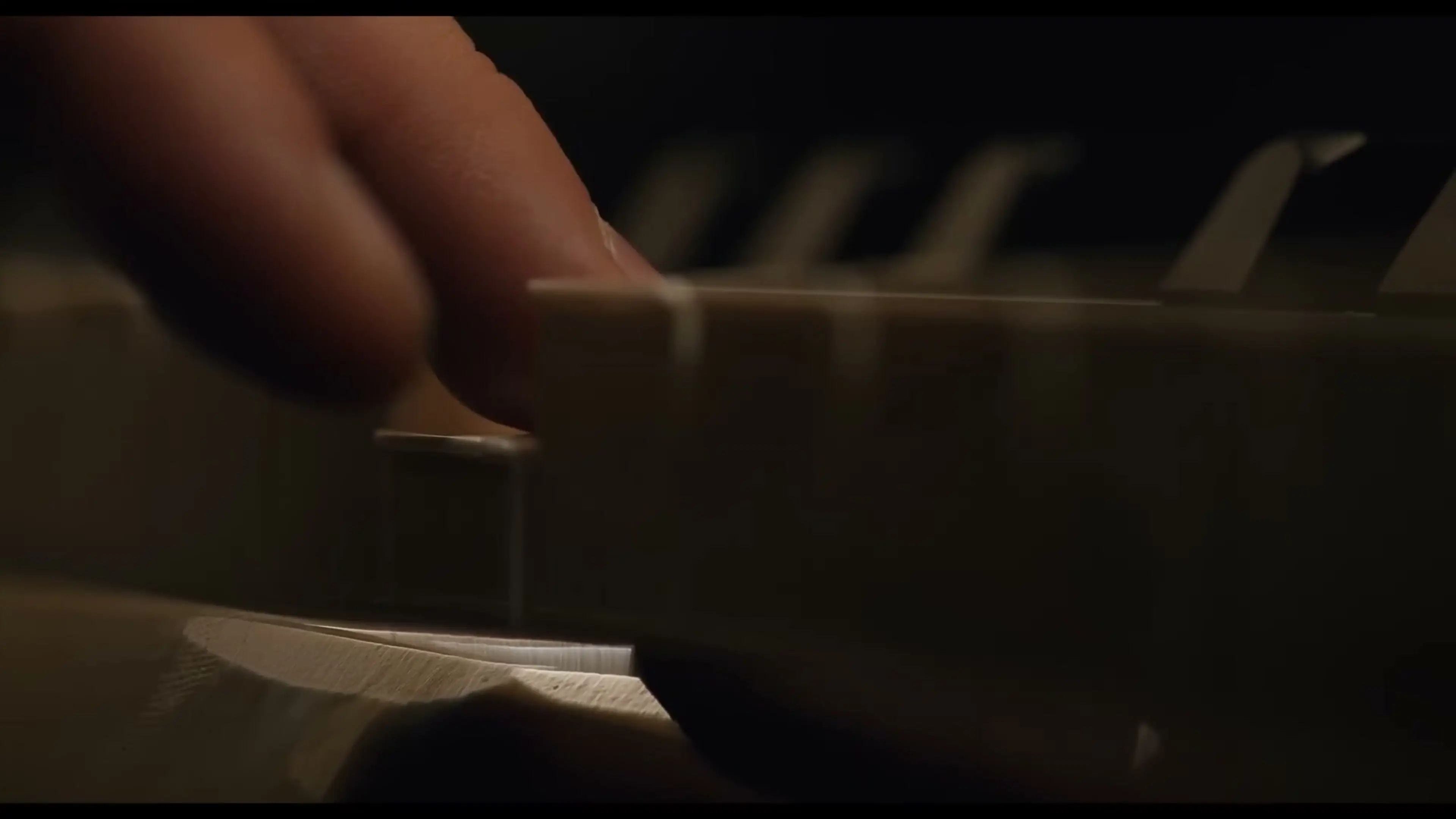 Fingers press the keys of a piano in close-up.