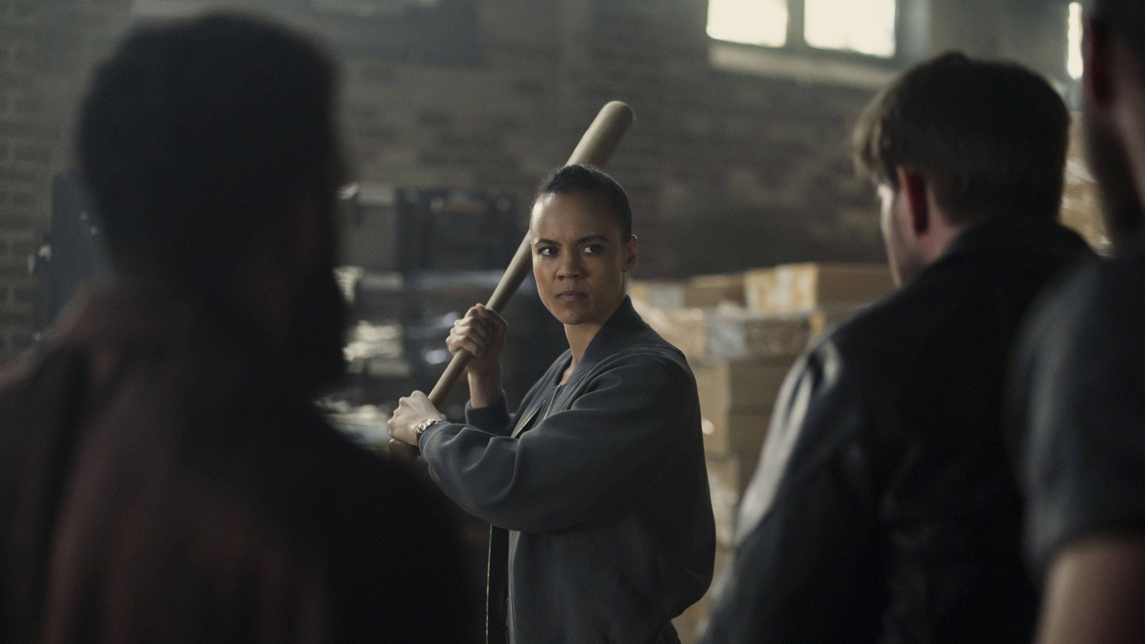 Frances Neagley holds a baseball bat while facing attackers in a warehouse.