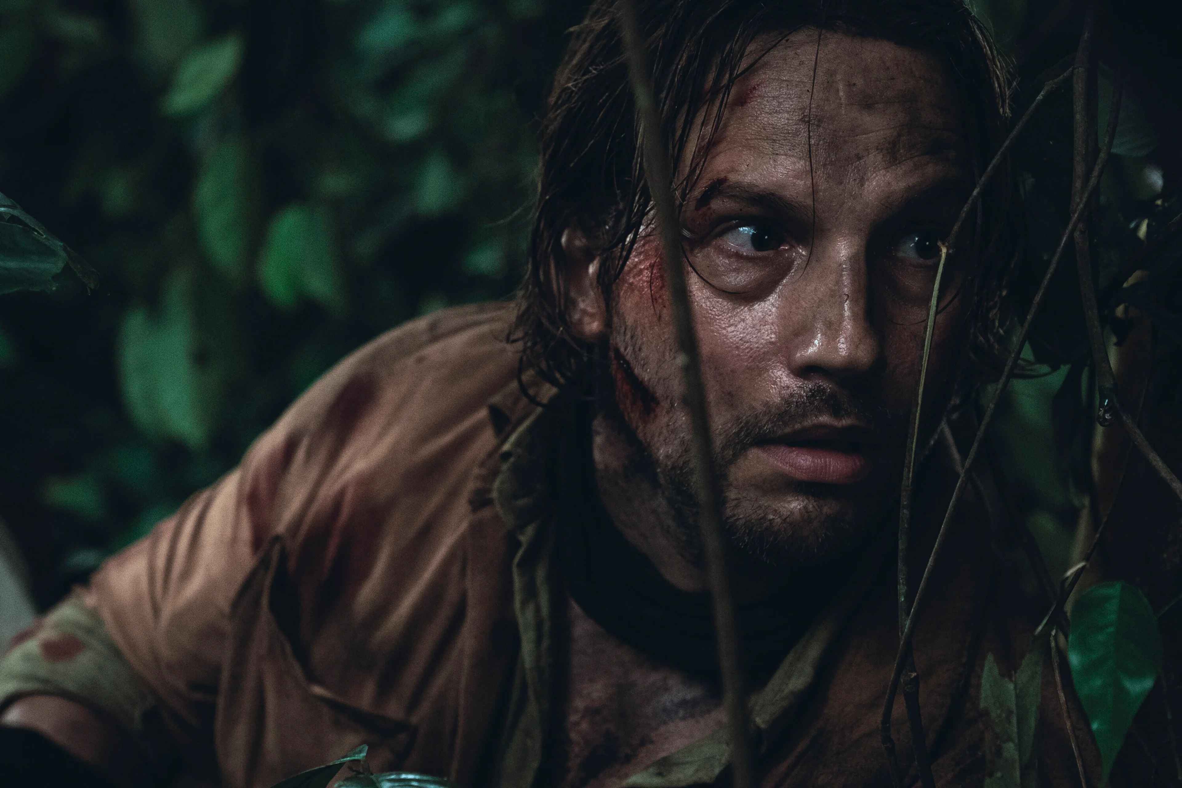 Logan Marshall-Green looks through vegetation in a Beware Boiúna production still.