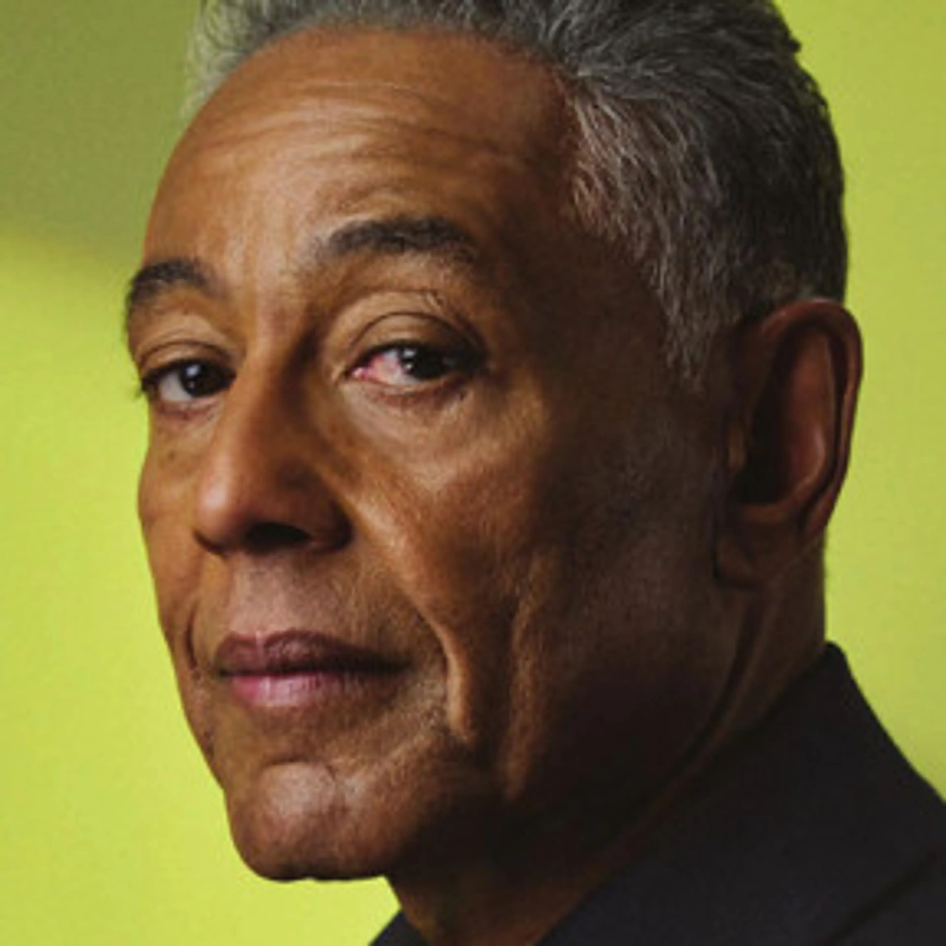 Portrait of Giancarlo Esposito in a dark shirt against a green background.