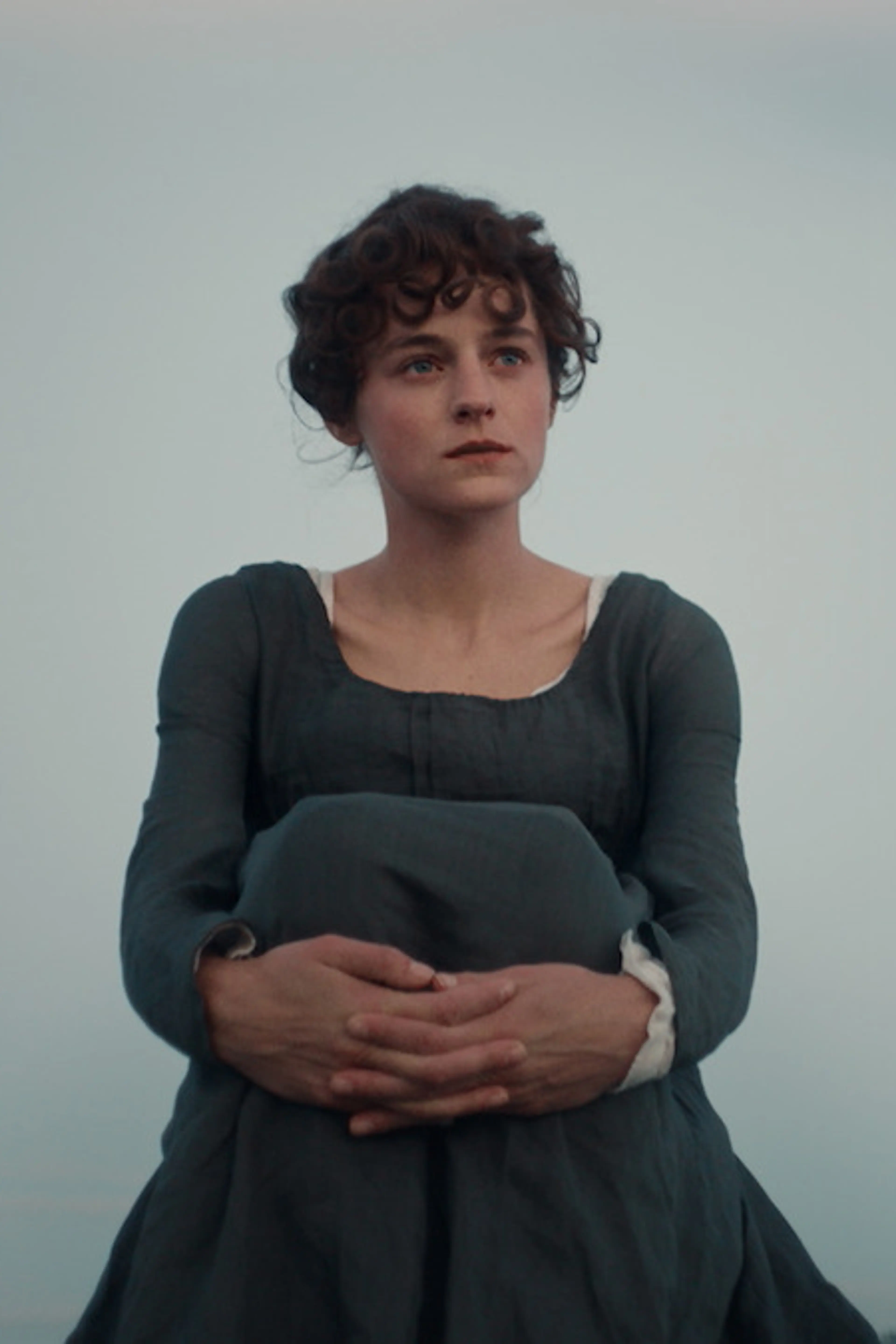 Emma Corrin sits outdoors in period costume as Elizabeth Bennet in Netflix’s Pride and Prejudice.