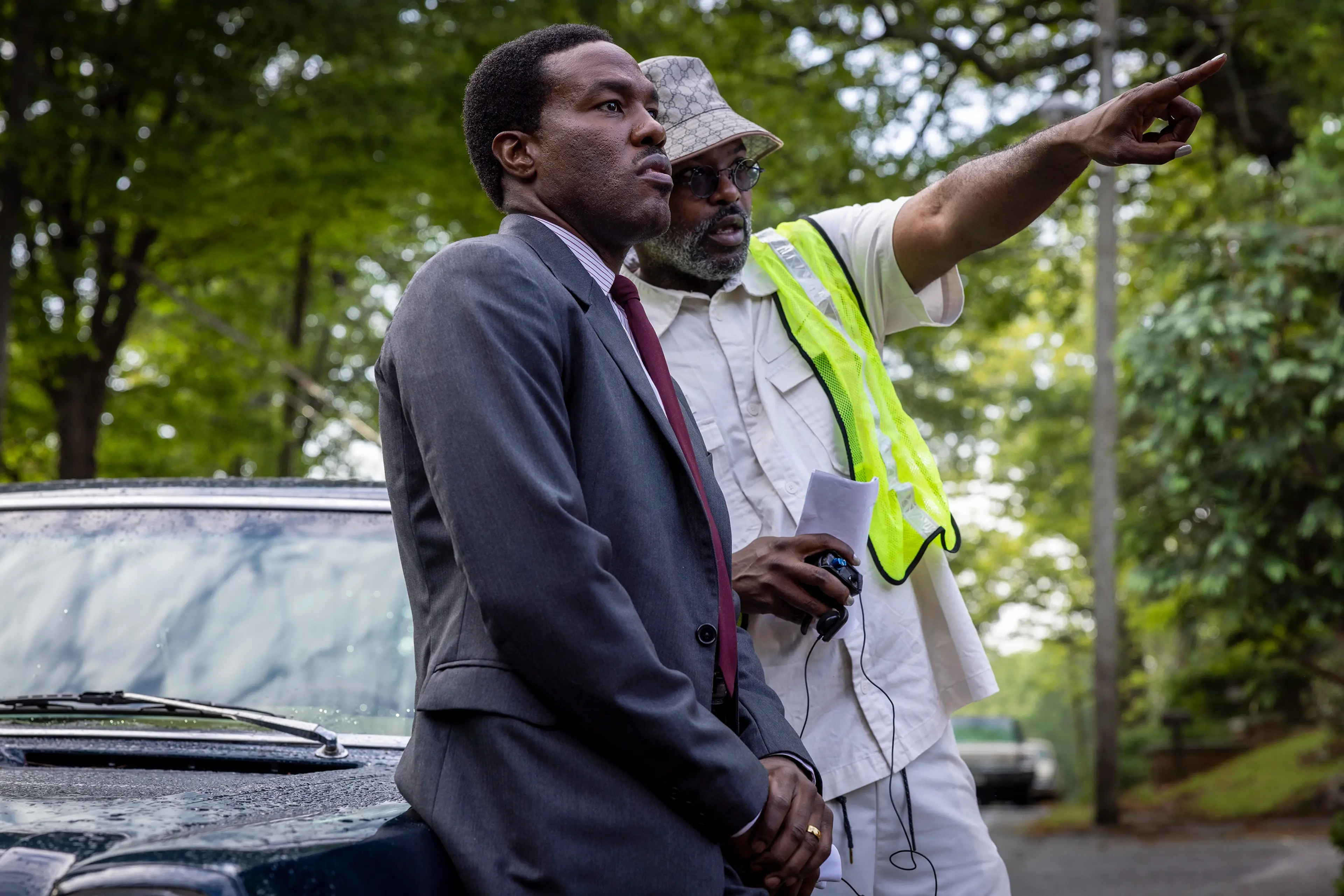 Director Elegance Bratton gives direction to Yahya Abdul-Mateen II beside a car on the By Any Means set.