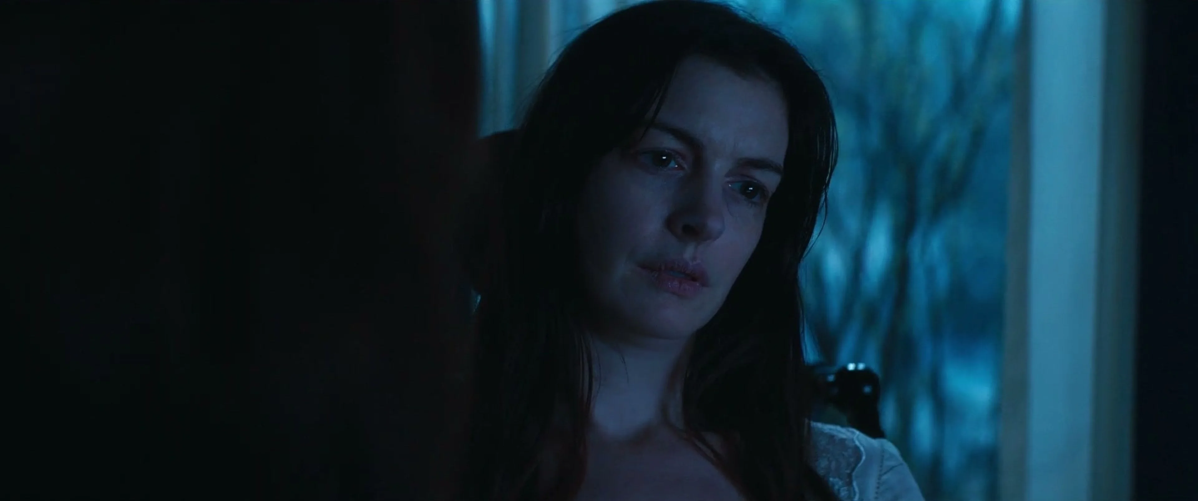 Verity sits with her head tilted, her face lit blue by the window behind her.