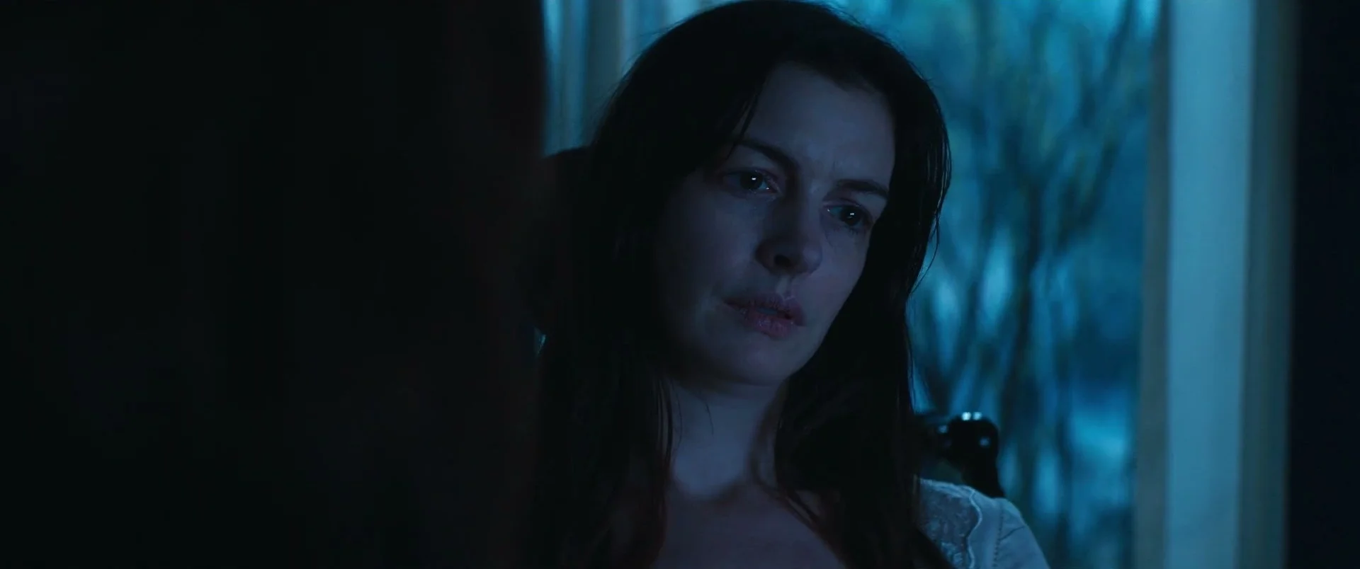 Verity sits with her head tilted, her face lit blue by the window behind her.