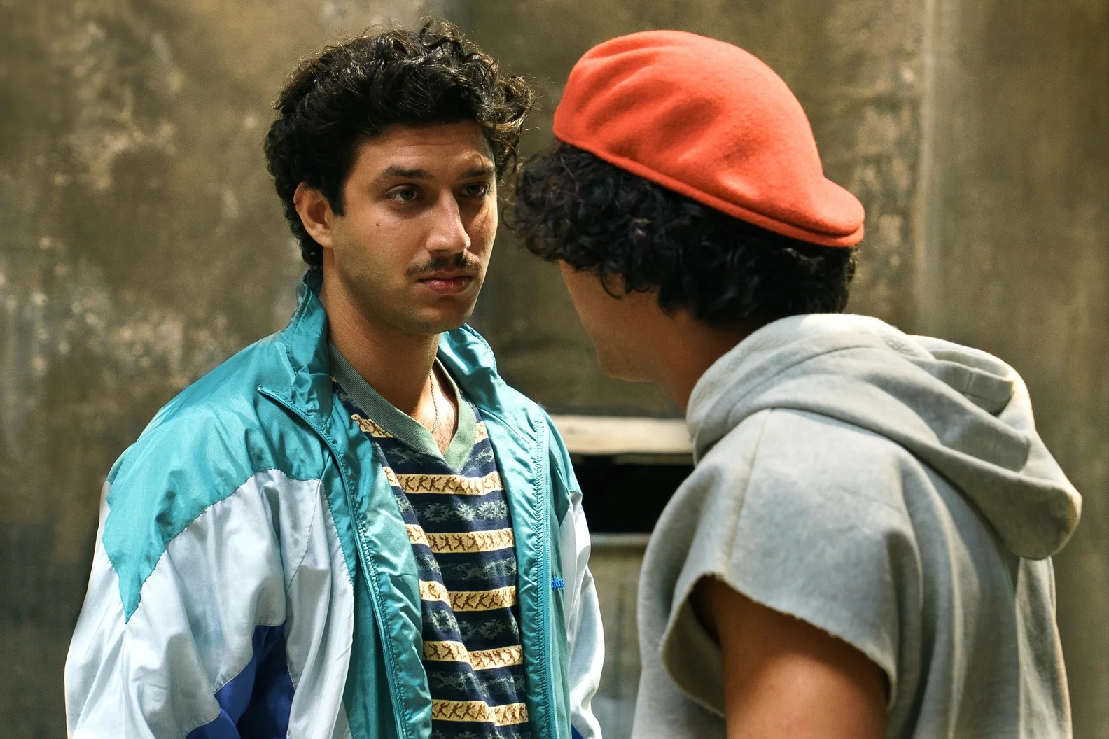 A young man in a blue jacket speaks with another man outdoors in 4 Blocks Zero Episode 2.