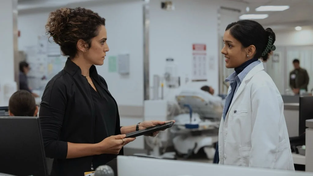 Two doctors talk beside a patient area in an official The Pitt Season 3 first-look image.
