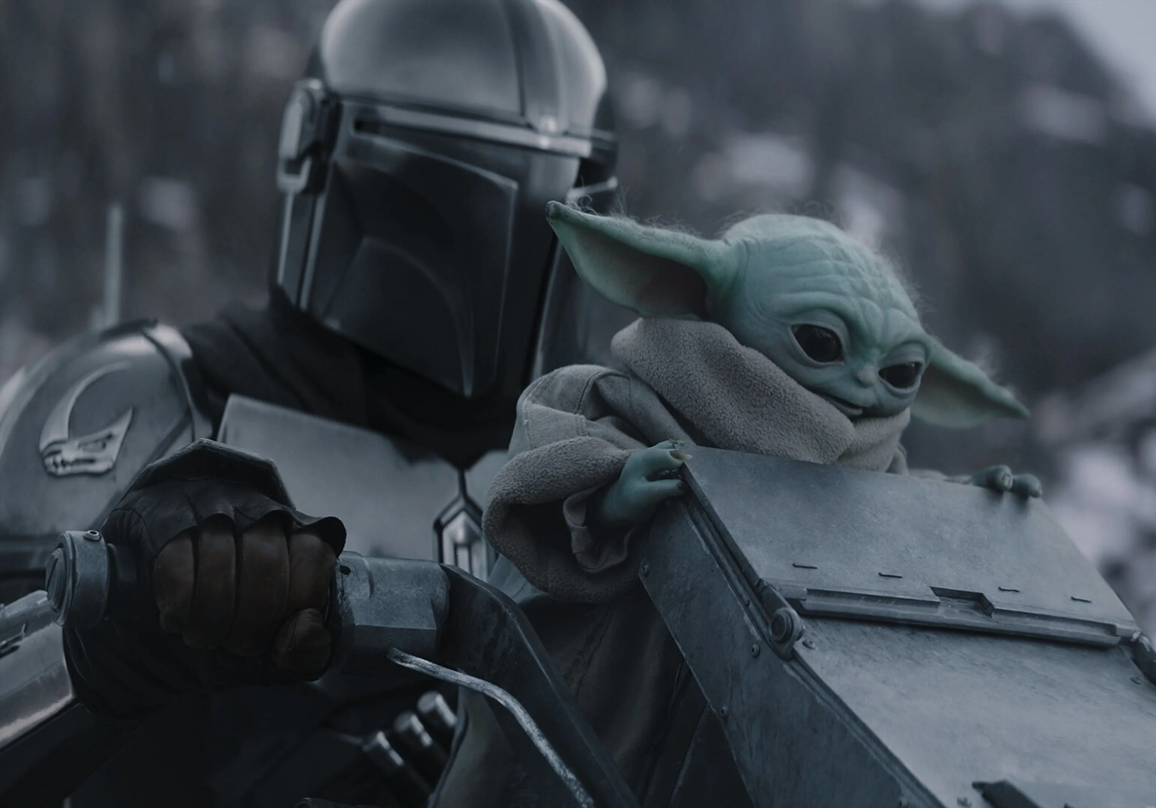The Mandalorian carries Grogu in an official still from Star Wars: The Mandalorian and Grogu.