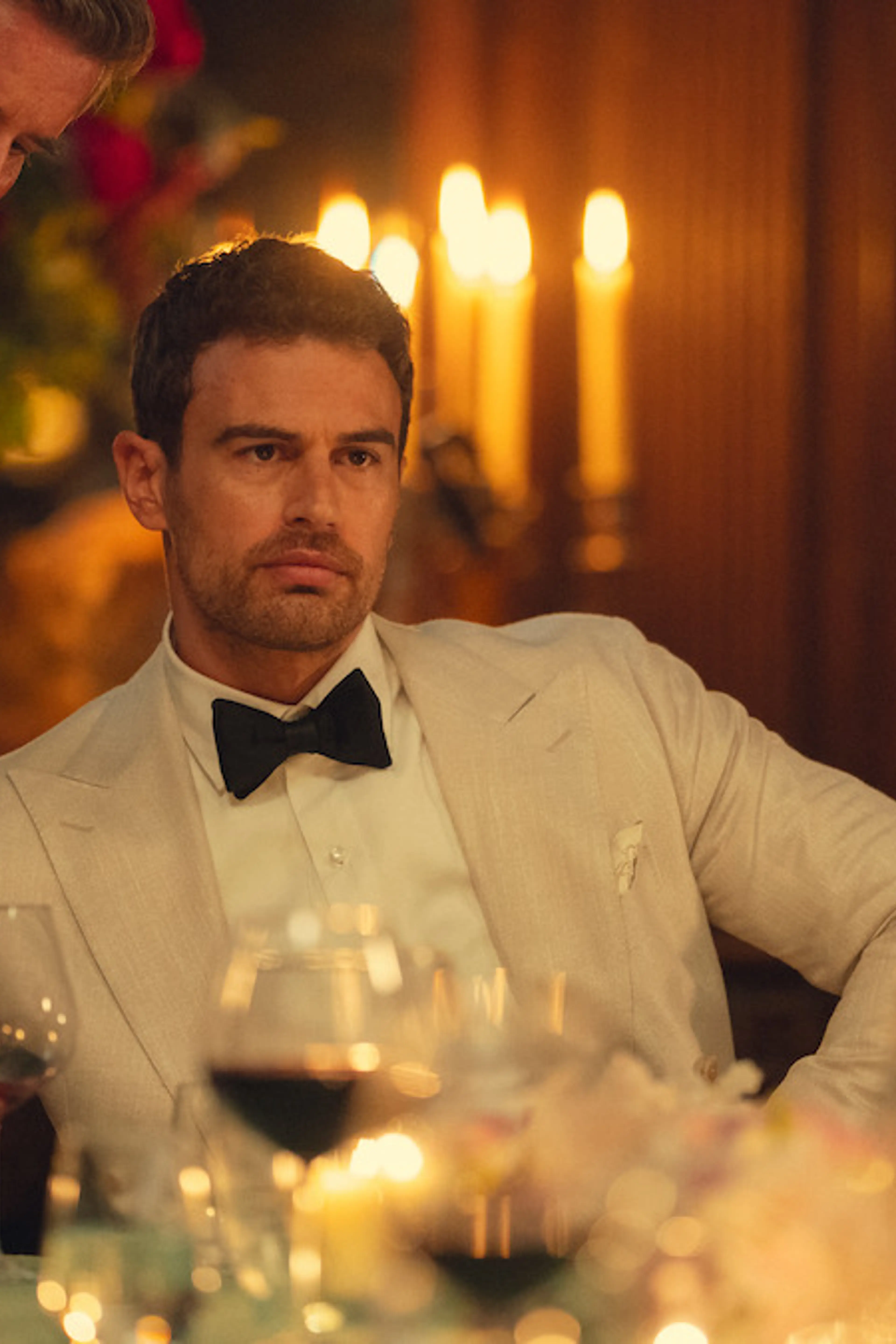 Theo James as Eddie Horniman sits at a candlelit dinner in The Gentlemen Season 2.