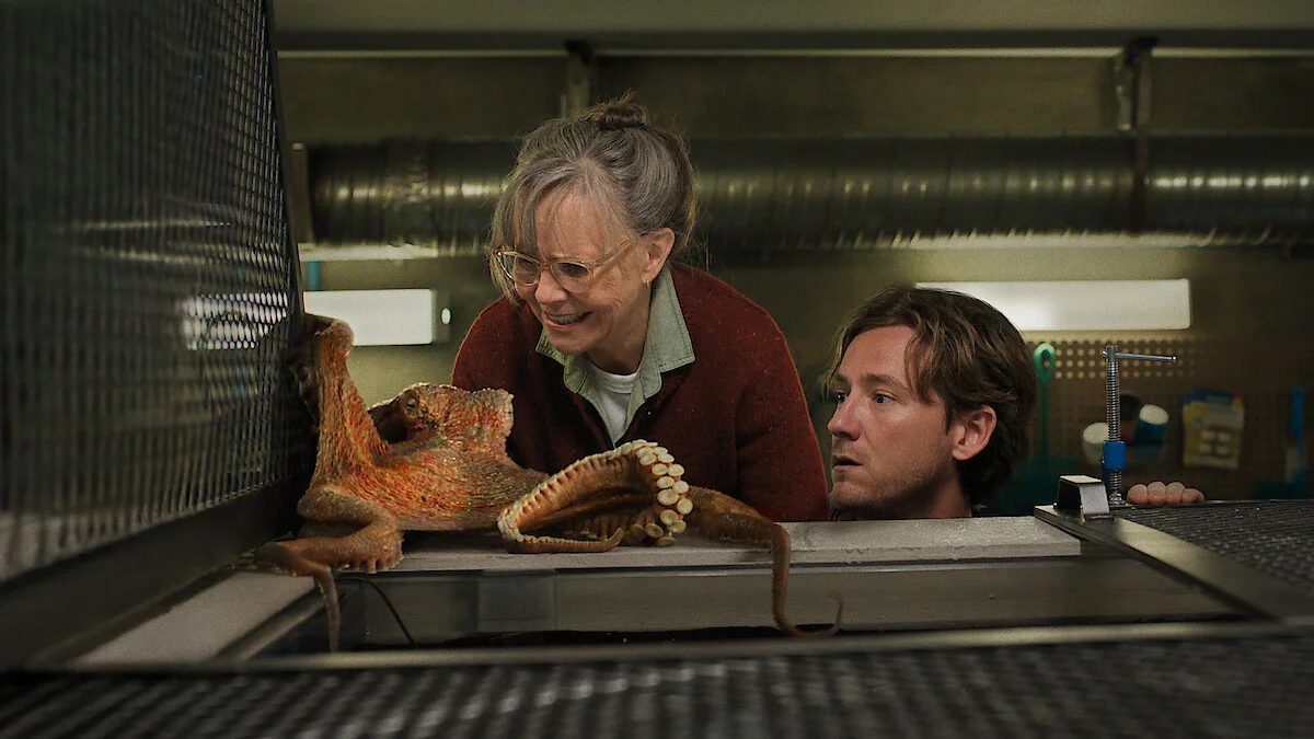Sally Field as Tova and Lewis Pullman as Cameron watch Marcellus move across an aquarium work surface.