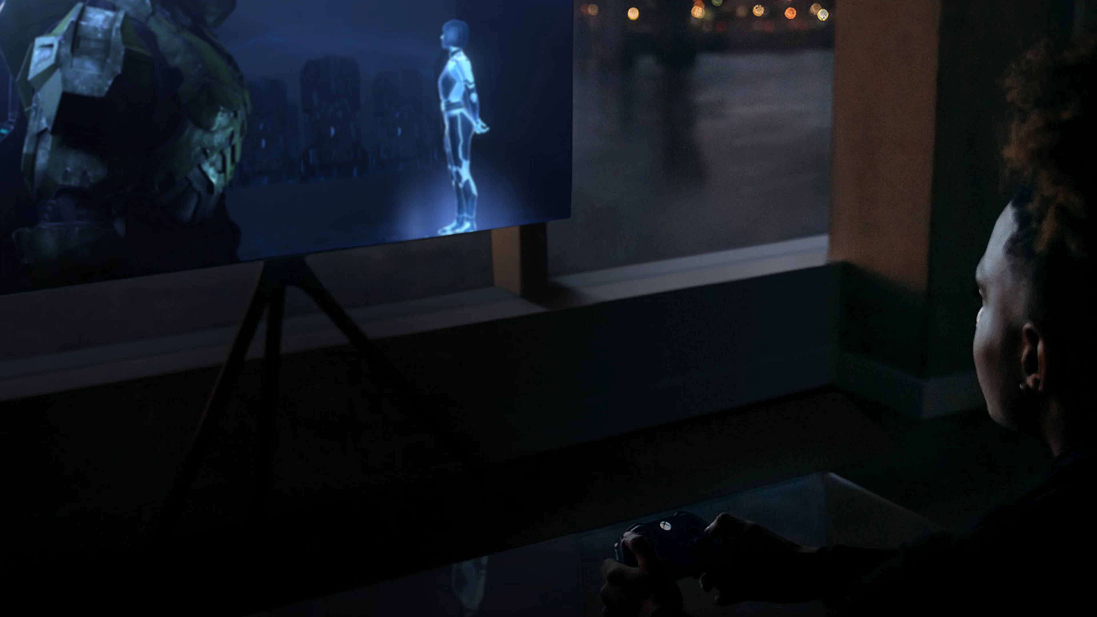 A player holds an Xbox controller while Halo streams on a television.