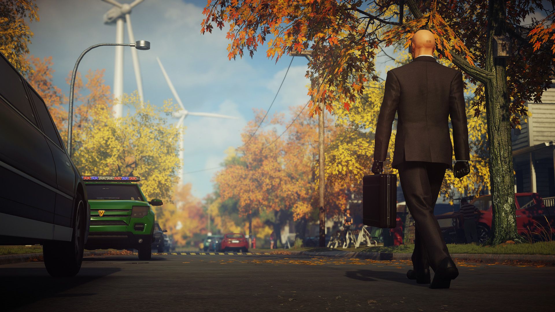 Agent 47 carries a briefcase down a quiet tree-lined suburban street.