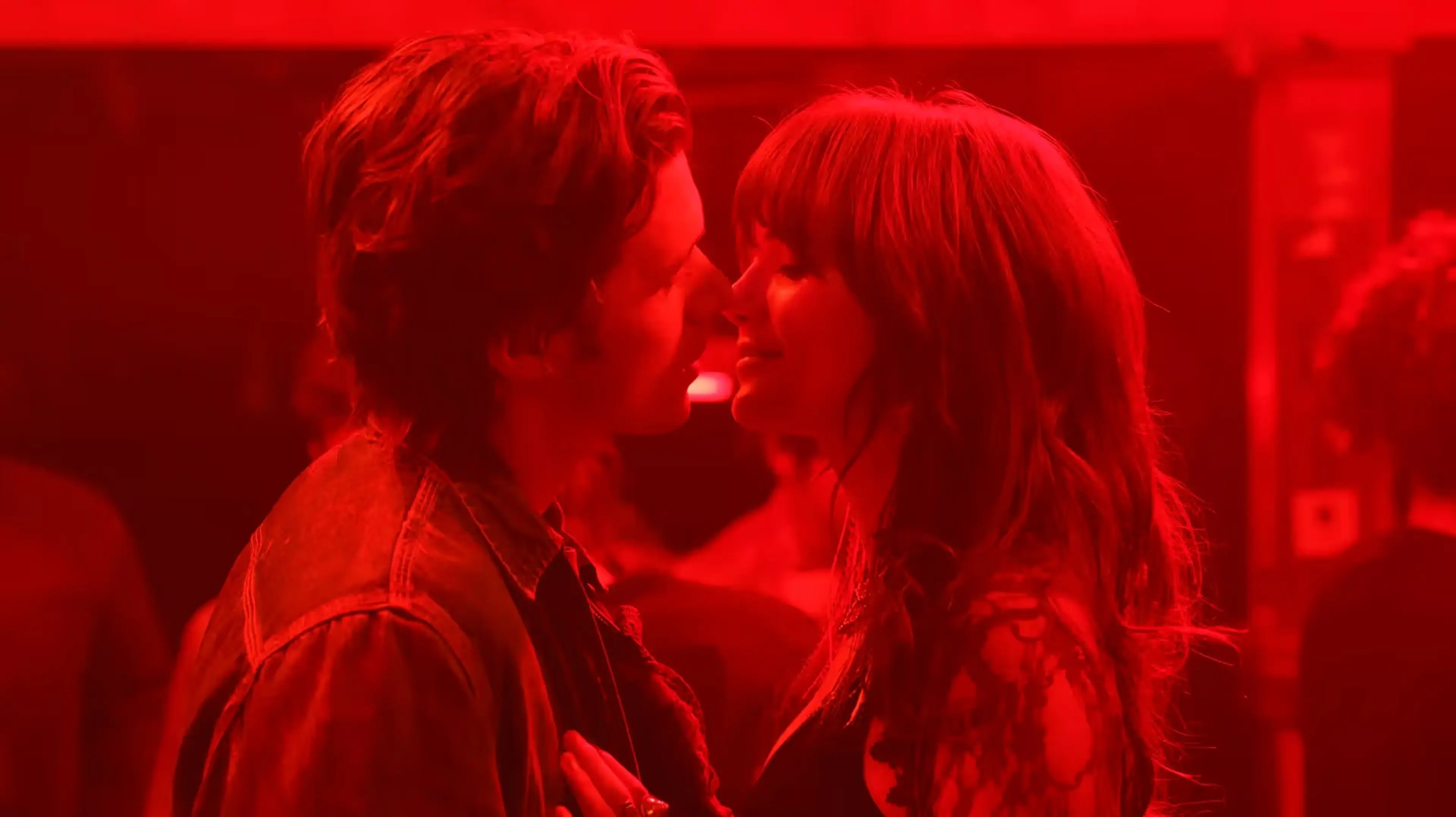Charlie and Harper face each other in a red-lit scene.