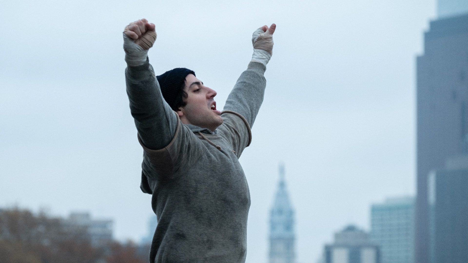 Anthony Ippolito as Sylvester Stallone raises his wrapped hands in an official I Play Rocky still.