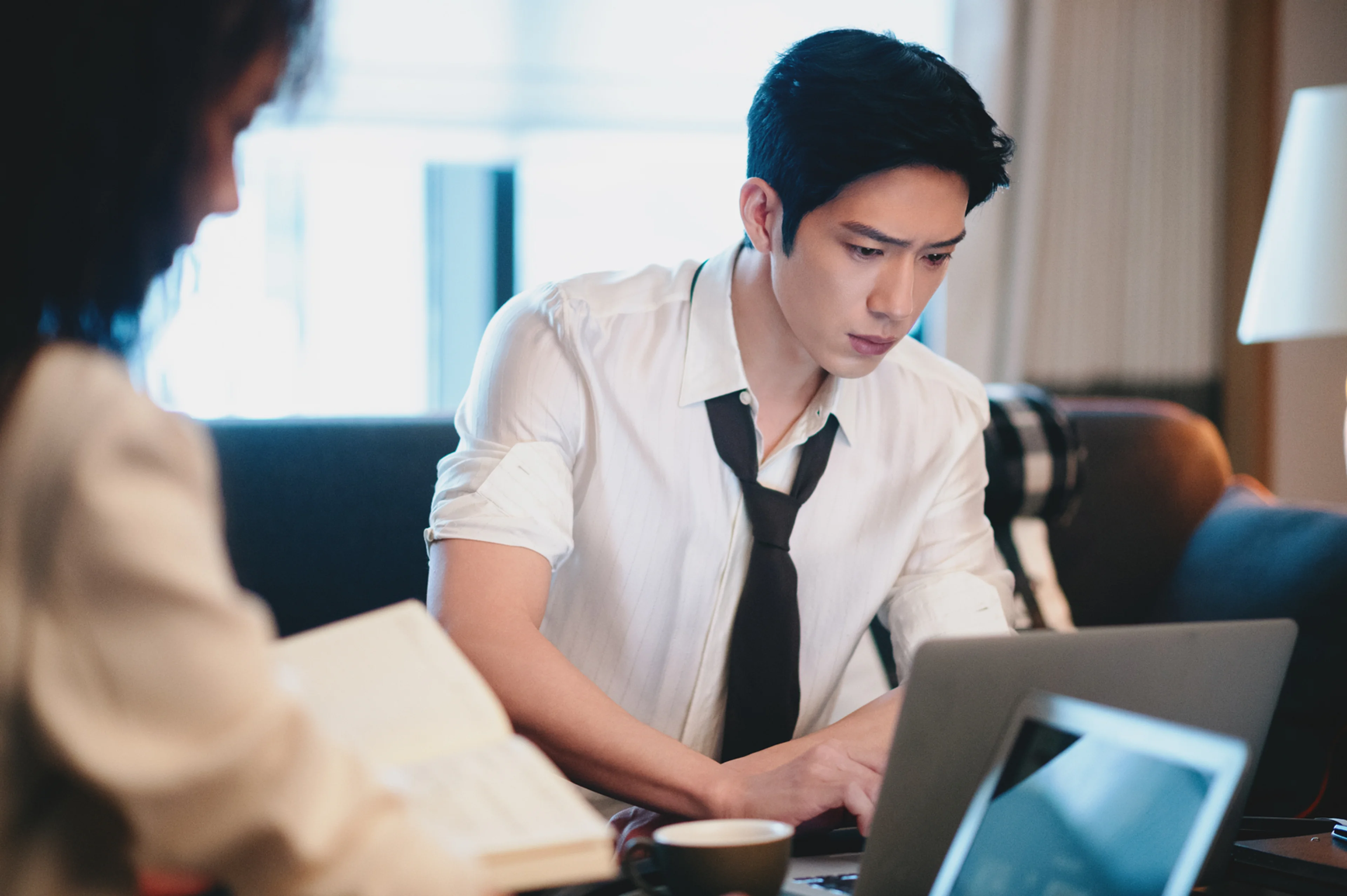 Jing Boran leans over a laptop in a white shirt with a loosened black tie.