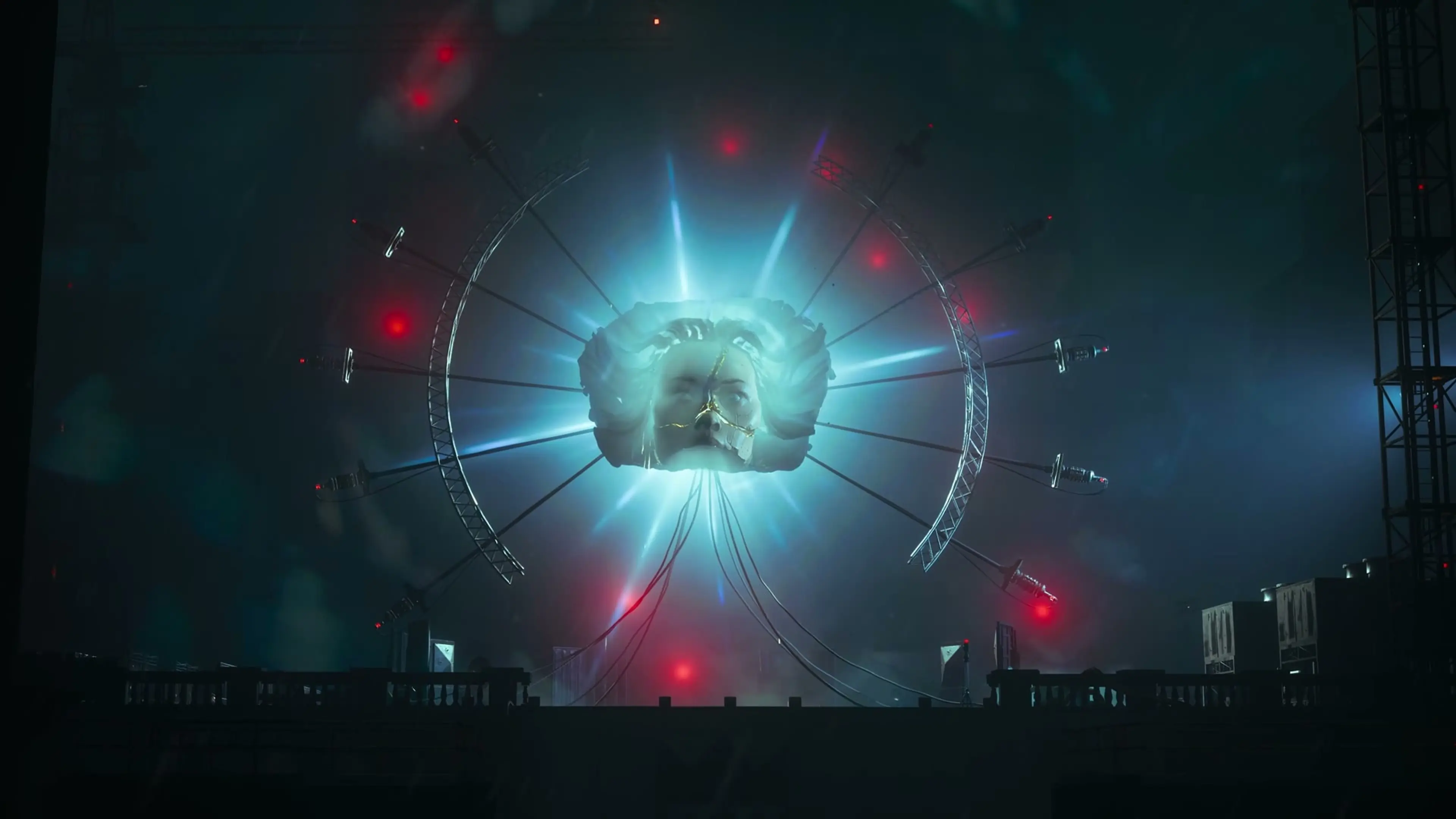 A large sculpted face hangs inside a circular structure with blue light and red lamps.