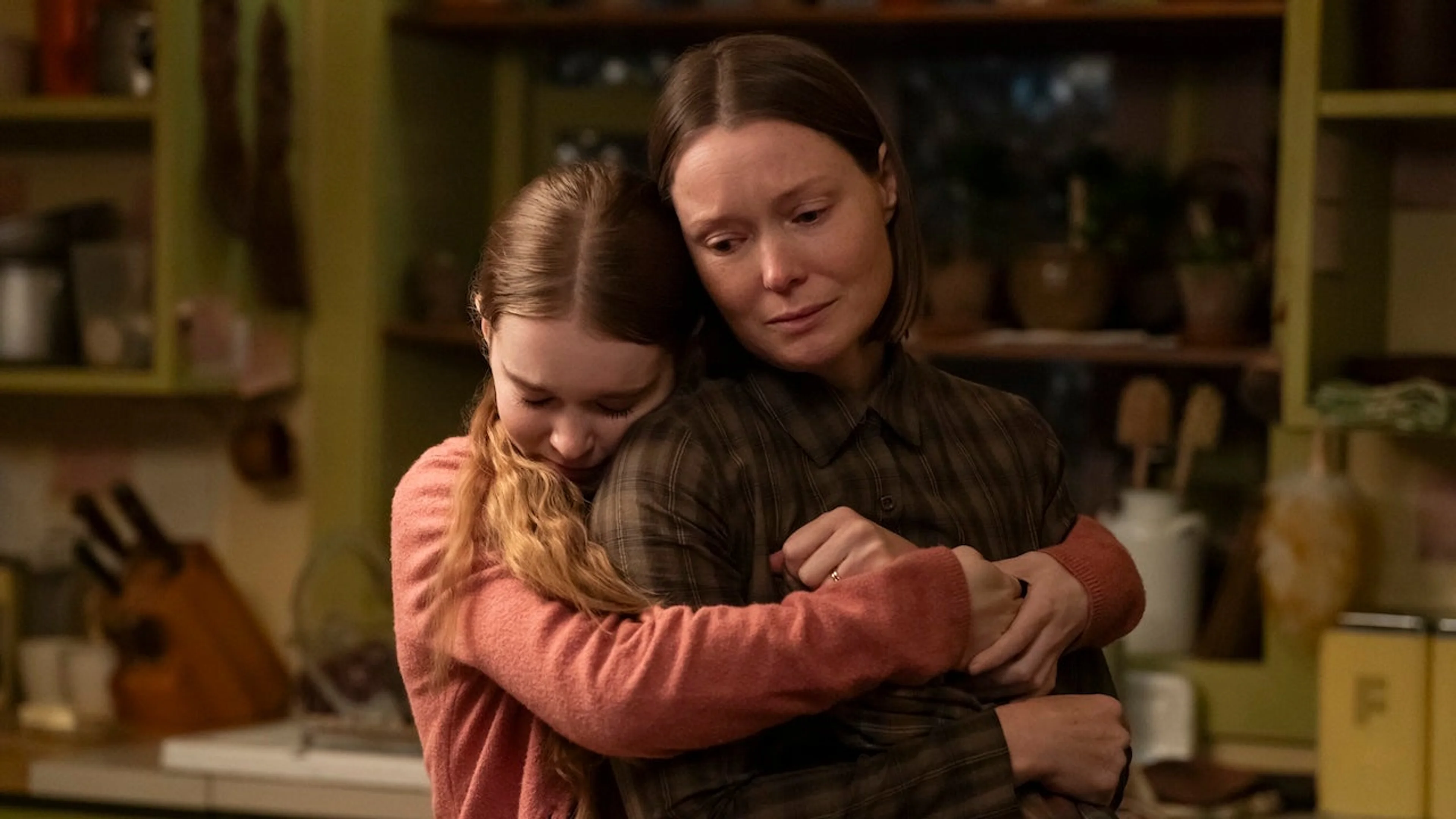 Margaret embraces Carrie in a kitchen while Carrie looks toward the camera.