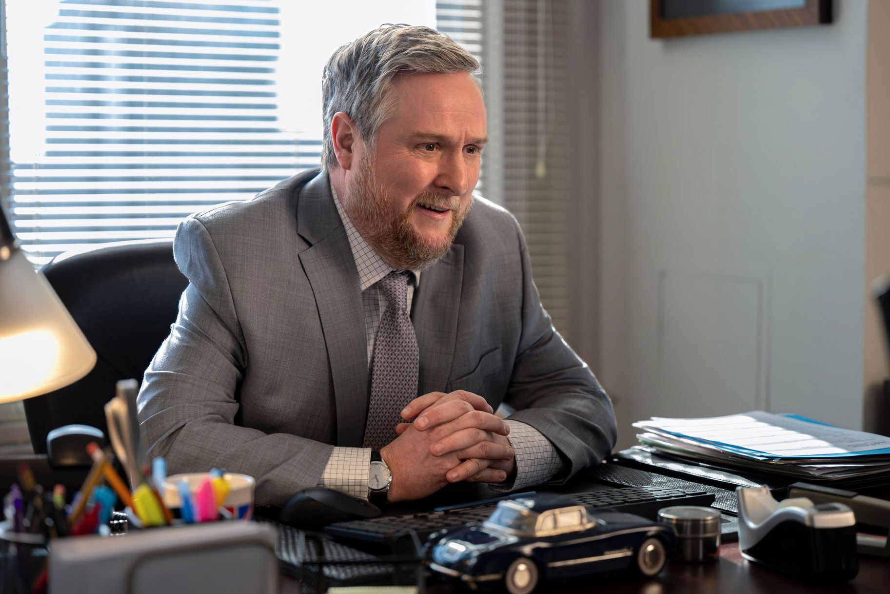 Ken sits at an office desk with his hands clasped.