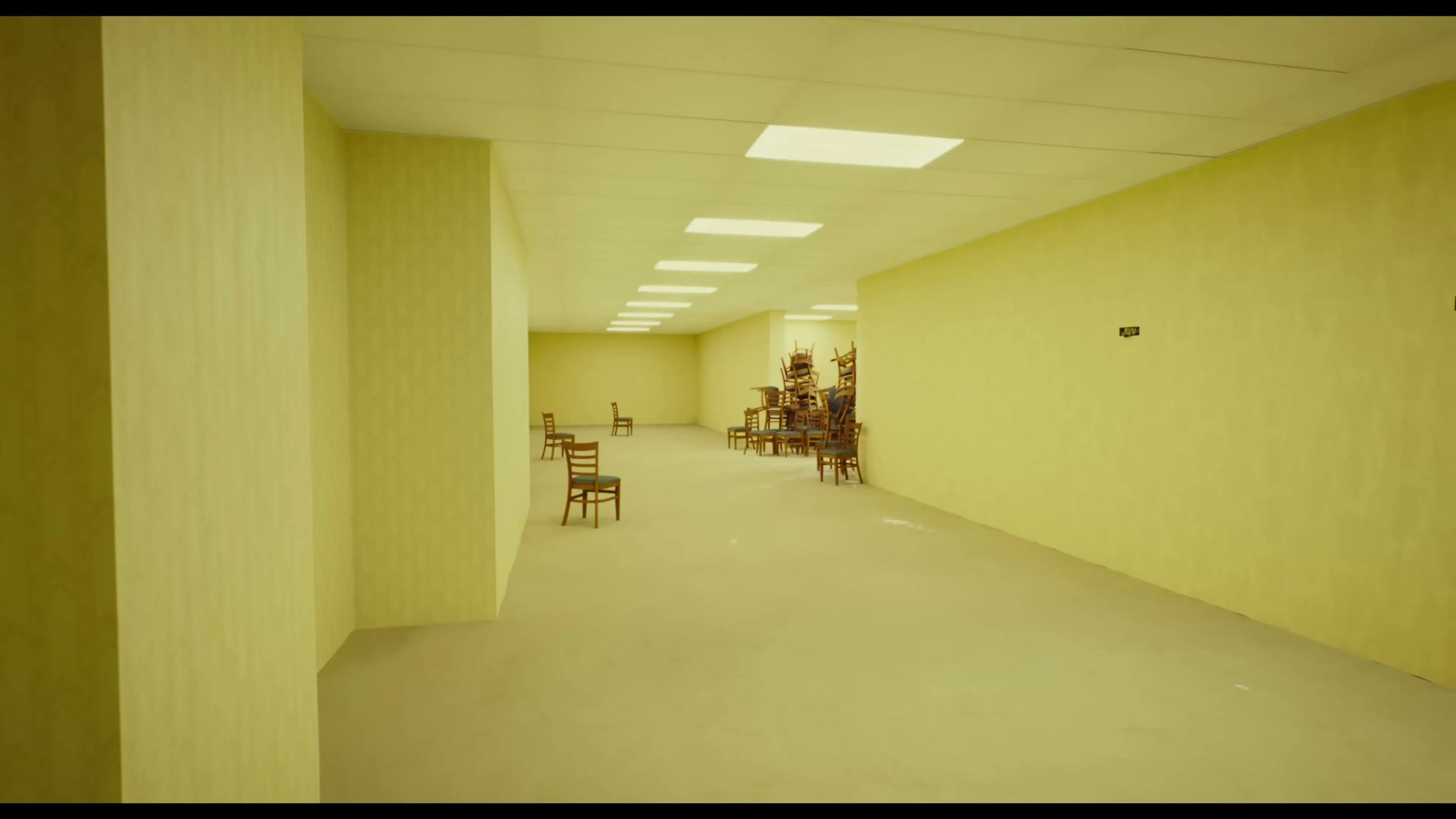Wooden chairs are scattered and piled up inside a long yellow room.