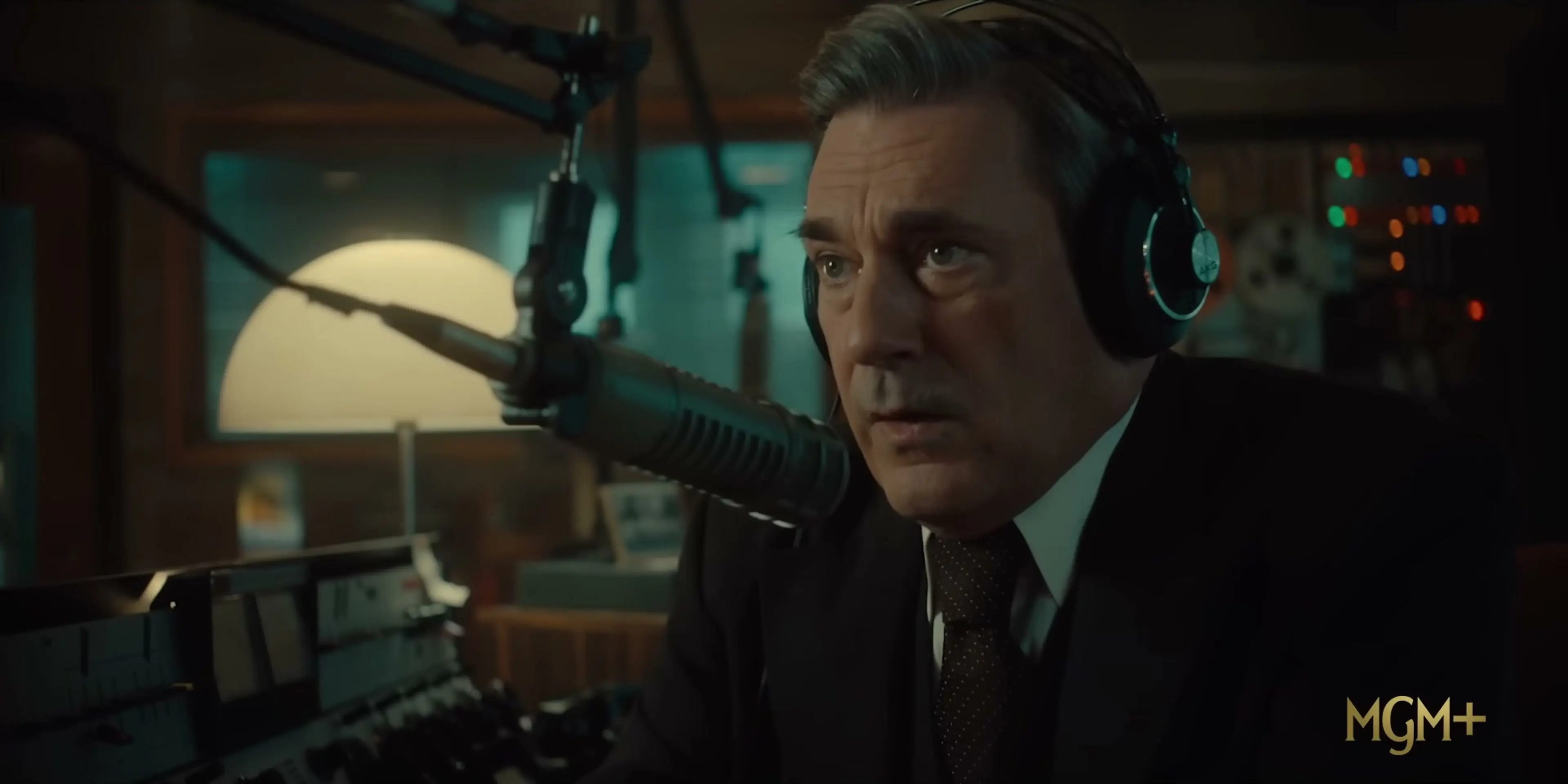 Jon Hamm as Fred Heckman listens through headphones inside a radio studio.
