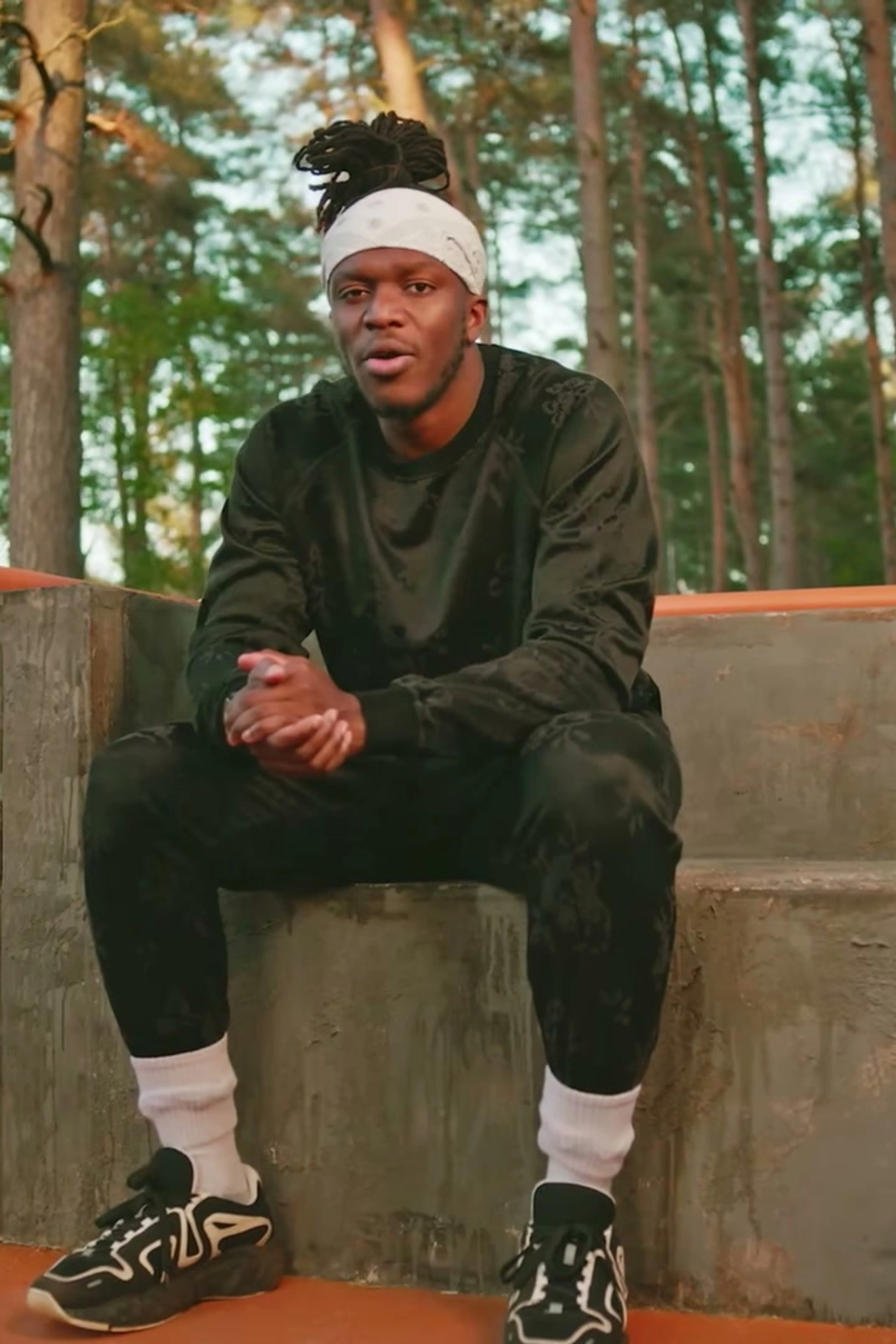 A Sidemen member sits on steps in the woods in the official Outside trailer.