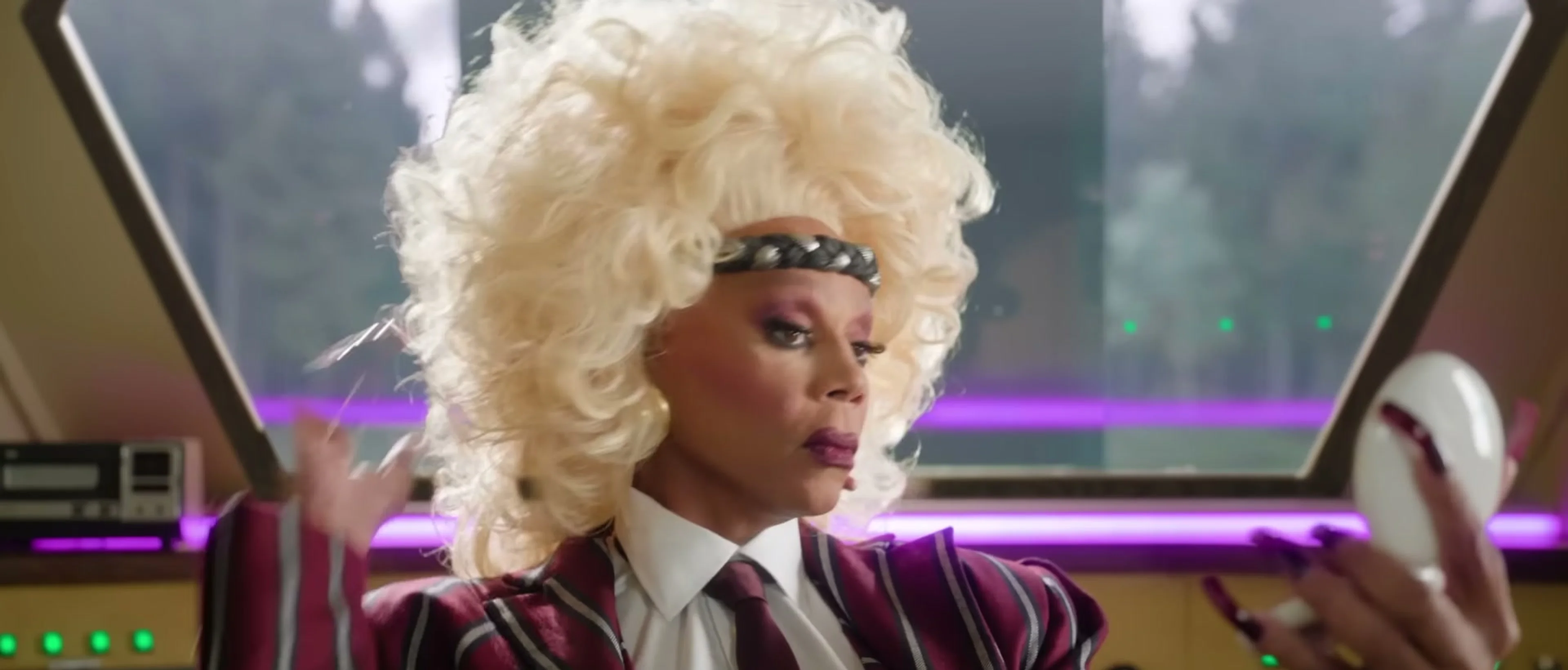 RuPaul in a blond wig looks at a mirror inside the train.