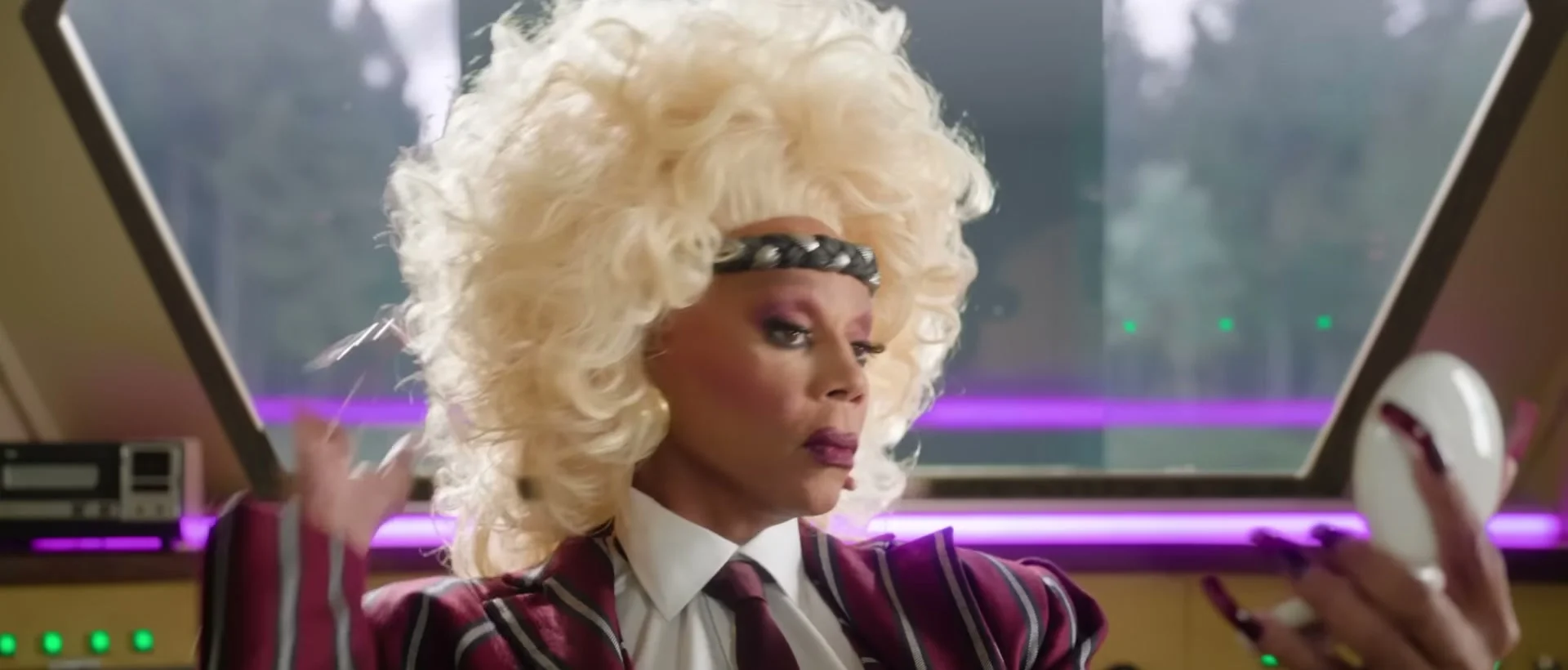 RuPaul in a blond wig looks at a mirror inside the train.
